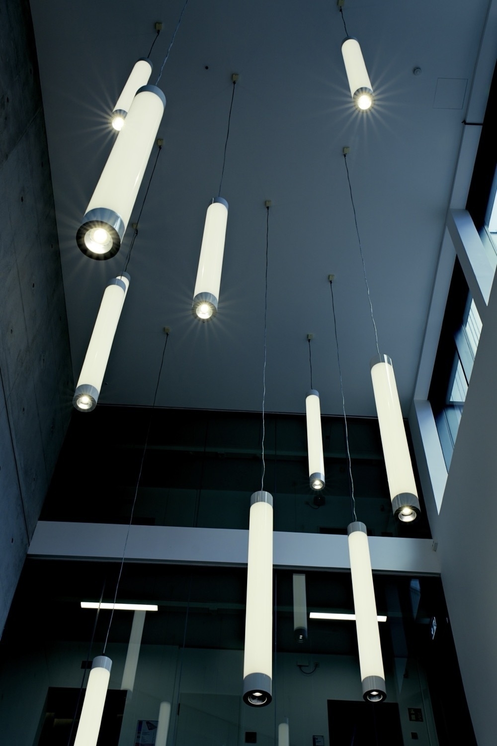 Several rod lamps hang from the ceiling at different heights in a multi-storey room. The lamps also have a spotlight facing down, from which the light radiates in the shape of a star.