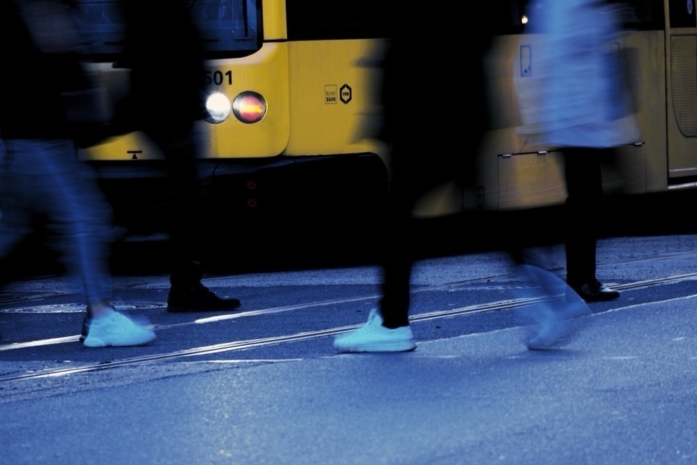 Legs of people crossing the street, with motion blur. A yellow tram in the background.