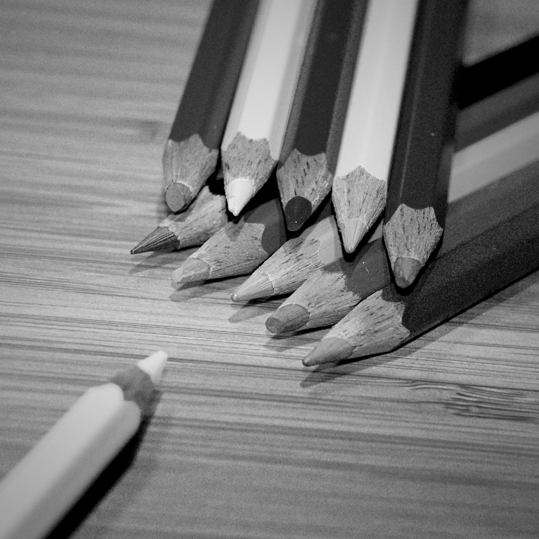 Black and white picture of colored pencils. At the top right, two rows of colored pencils lie on top of each other, another one protrudes into the picture from the bottom left.