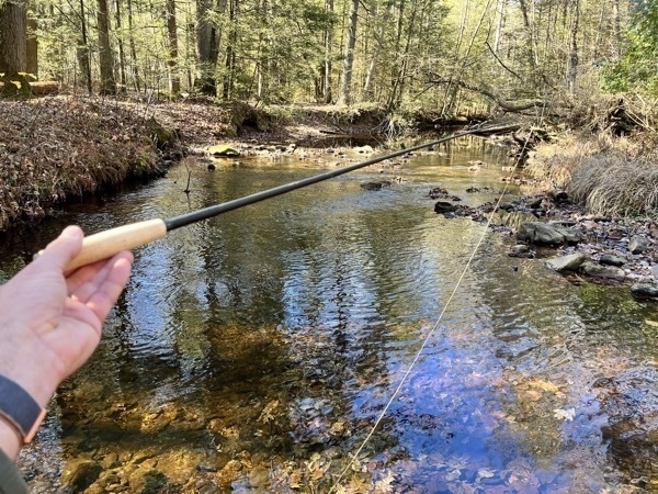 Tiny tenkara rod in hand, with stream in background