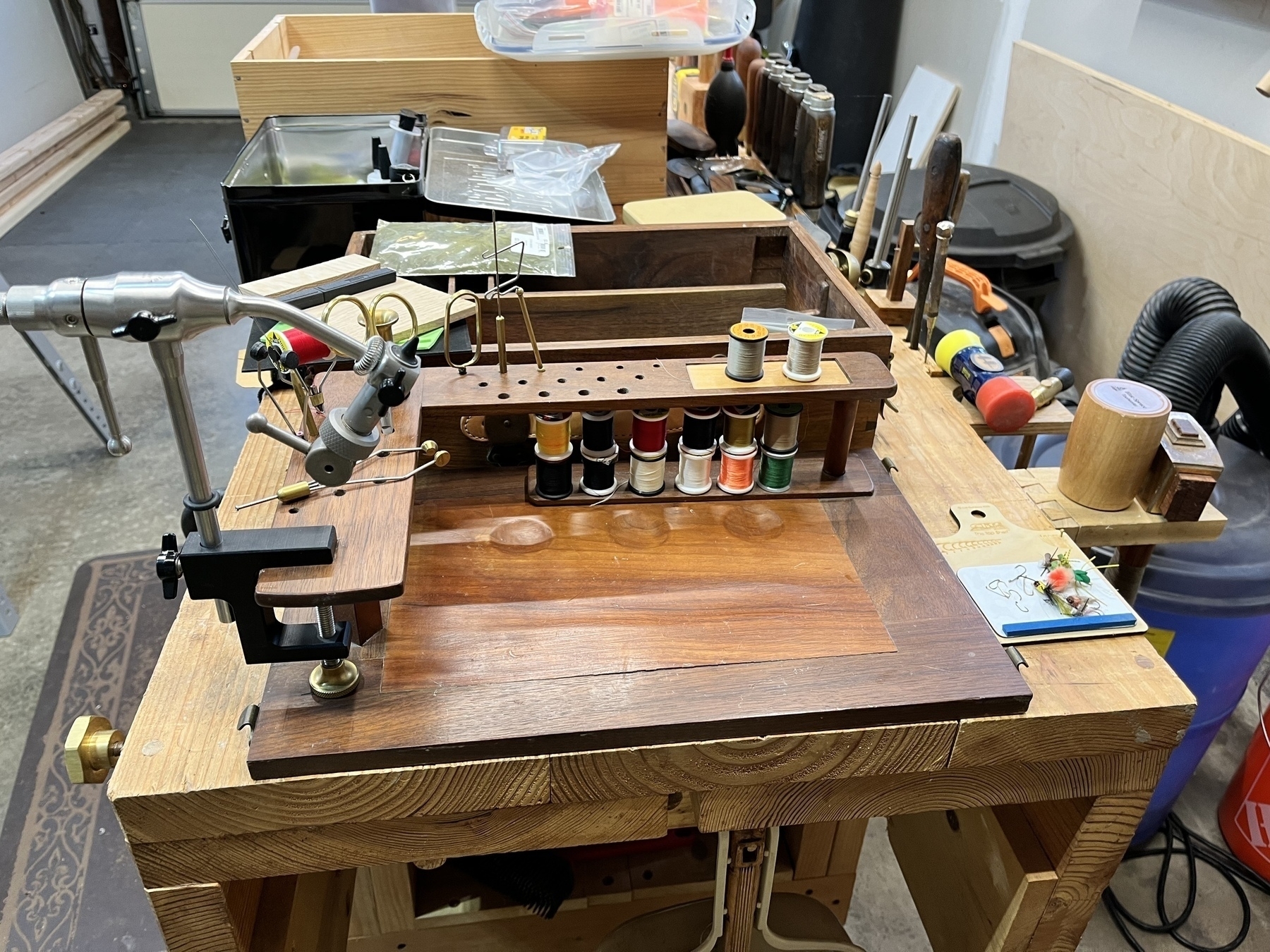 A fly tying station features various tools, spools of thread, and organized compartments on a wooden woodworking workbench.