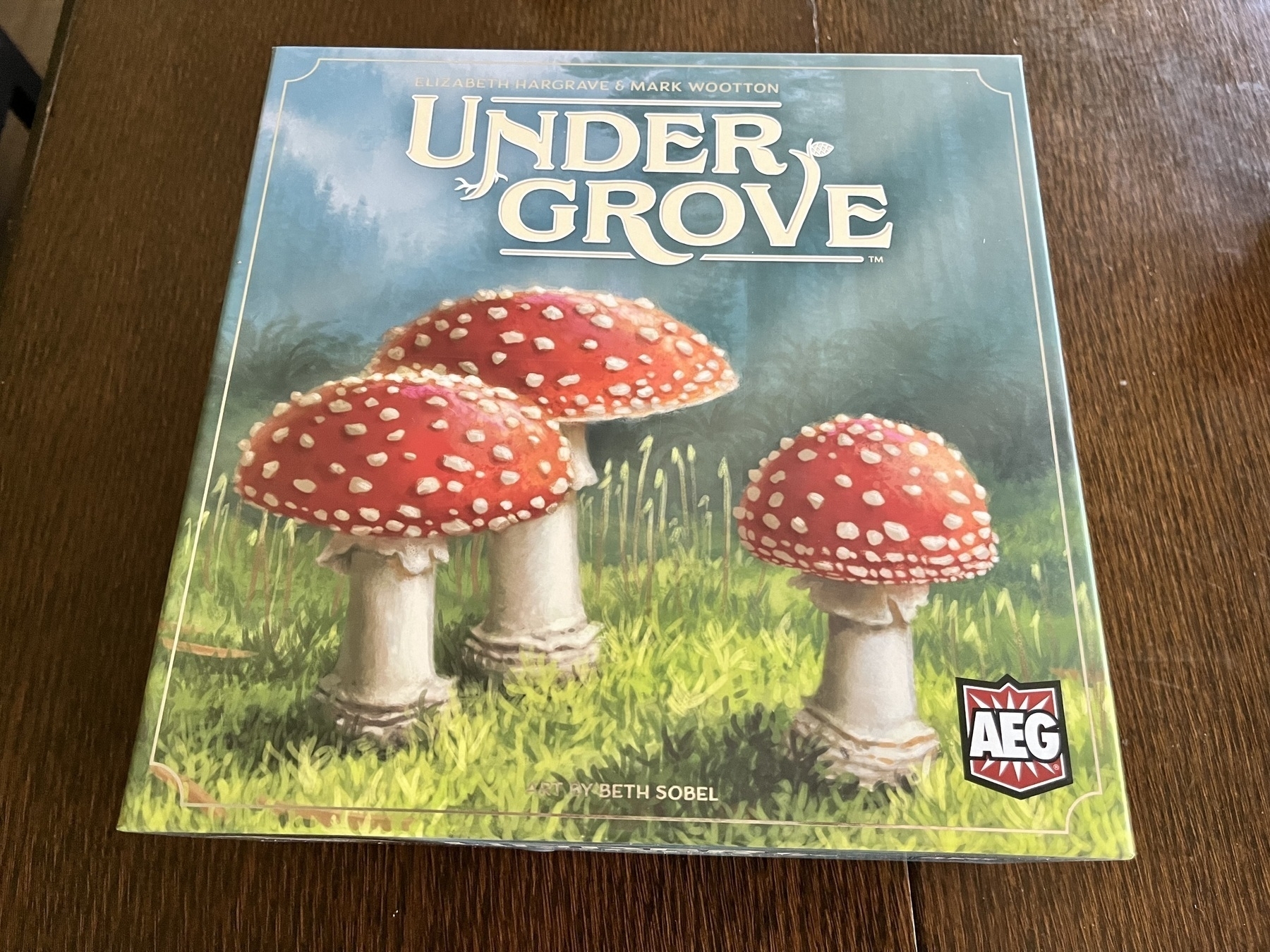 The image shows a board game box titled "Undergrove," featuring an illustration of three red mushrooms with white spots on grass, set against a forested background.