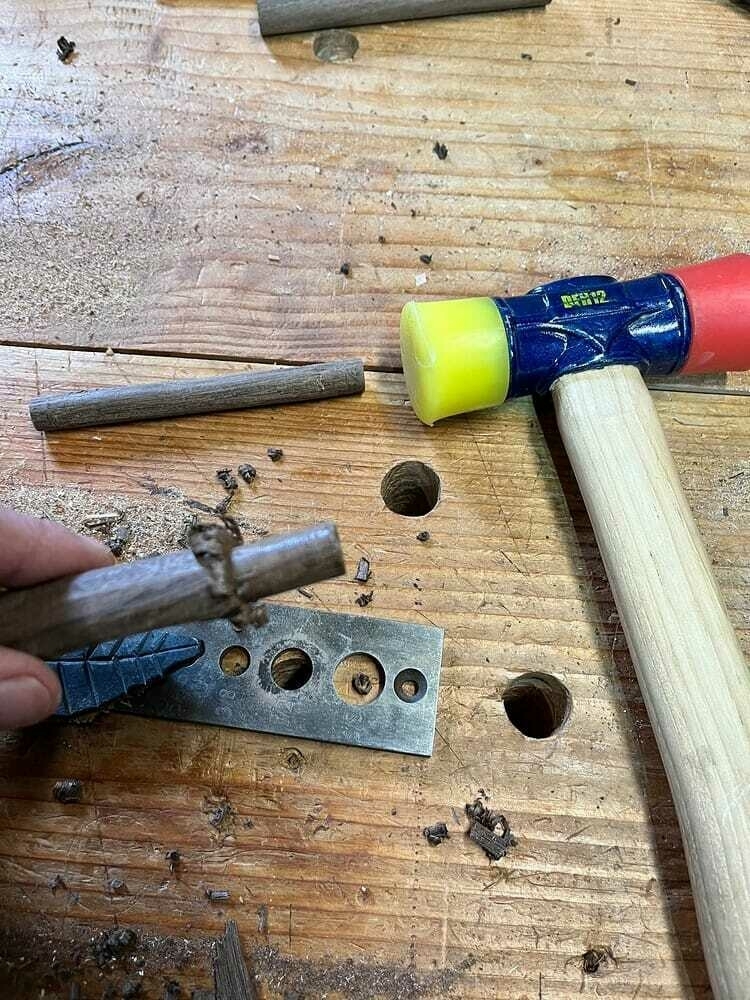 a partially handcut walnut dowel with a jig and hammer used to pound it out.