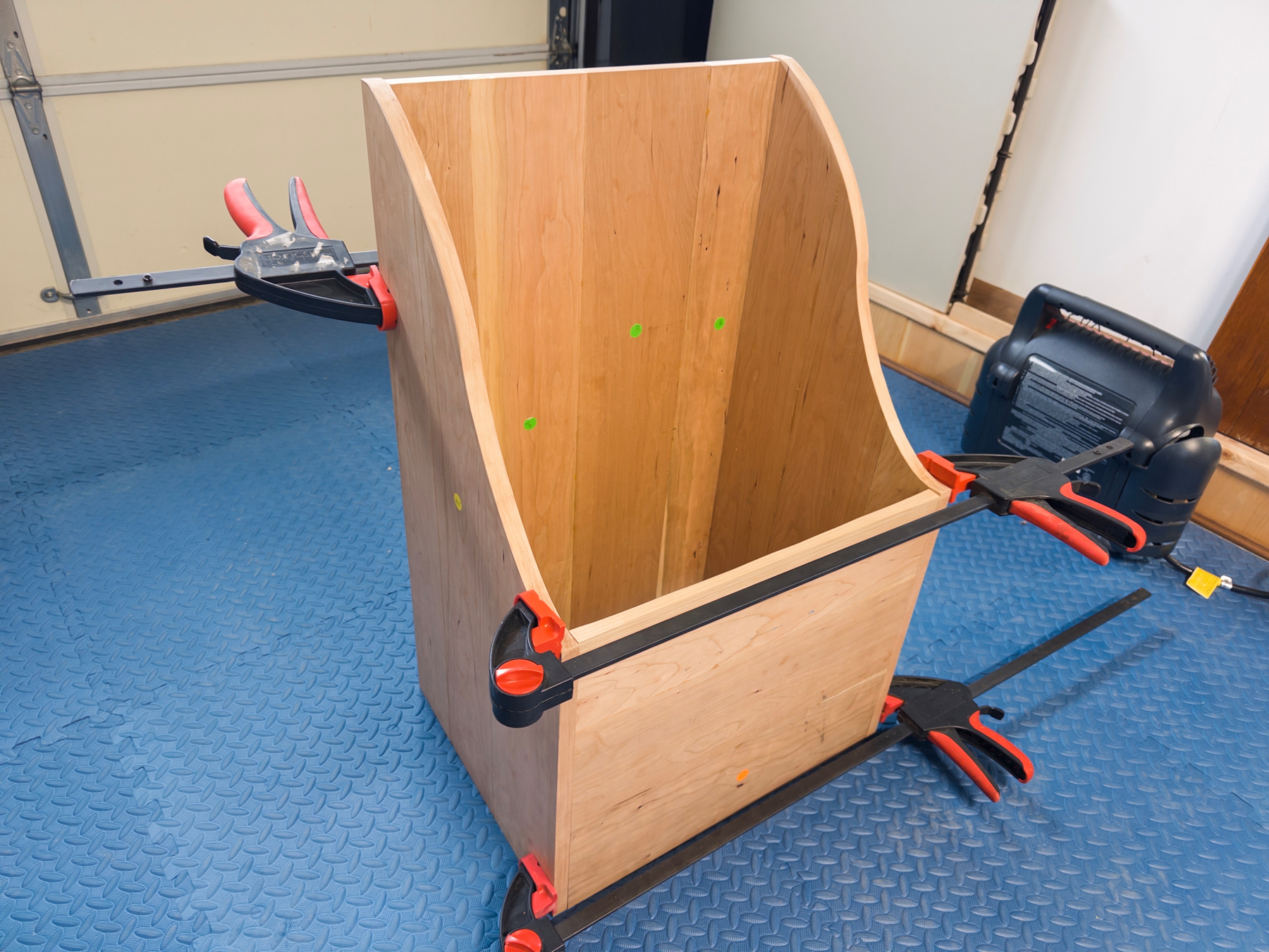 A cherry wood firewood box is being assembled with clamps in a workshop.