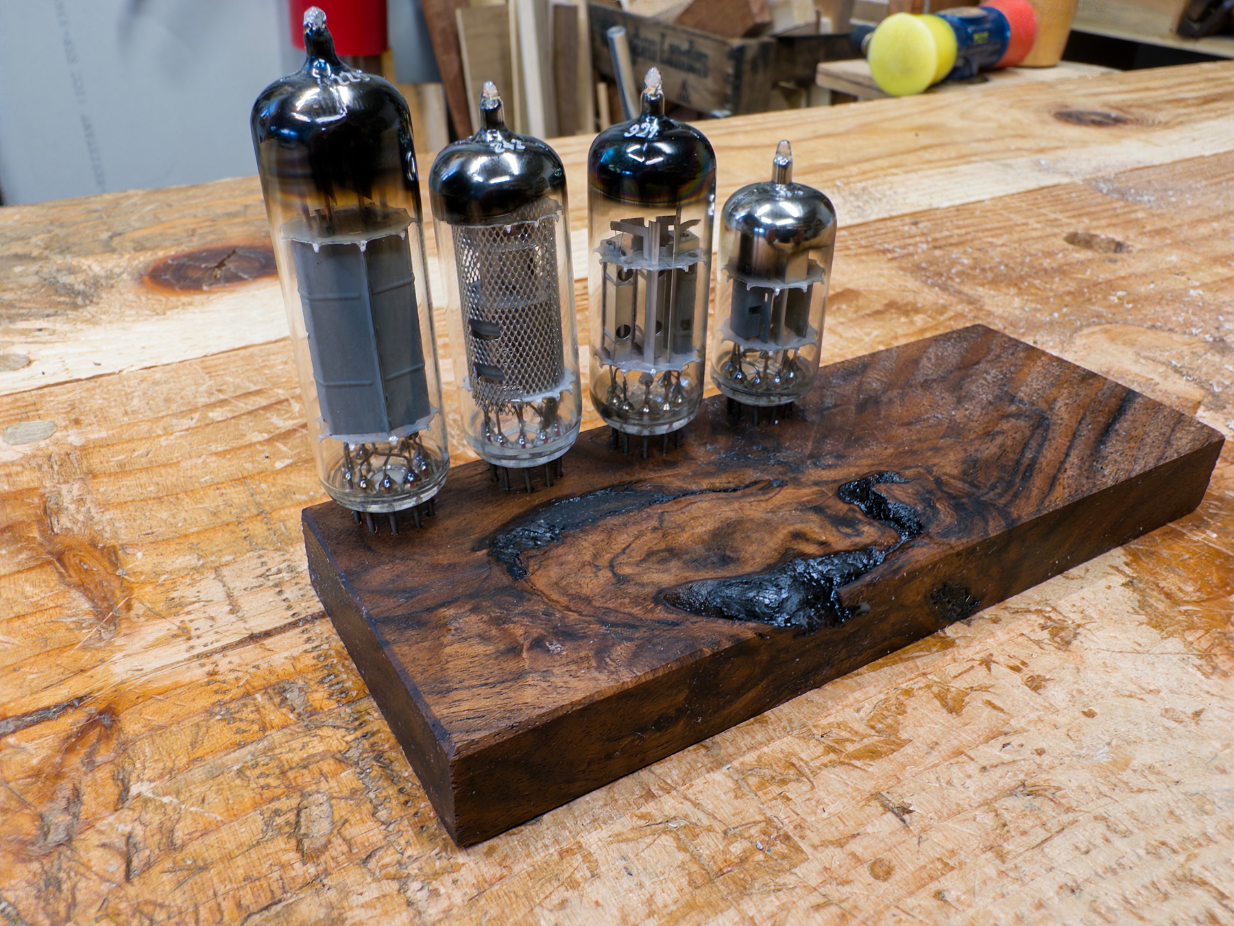 Four vacuum tubes are displayed on a wooden block resting on a workbench.