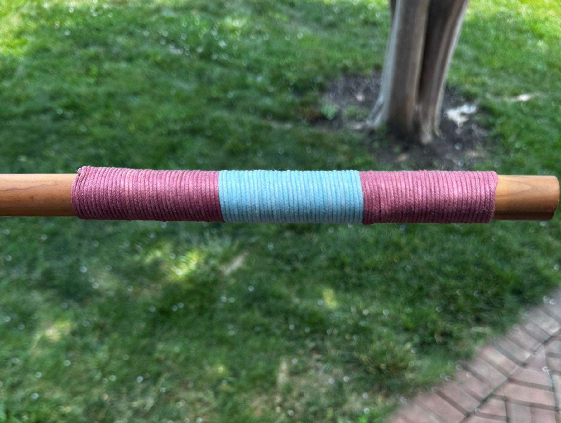 The handle of a wooden tool wrapped in multiple colors of waxed cord.