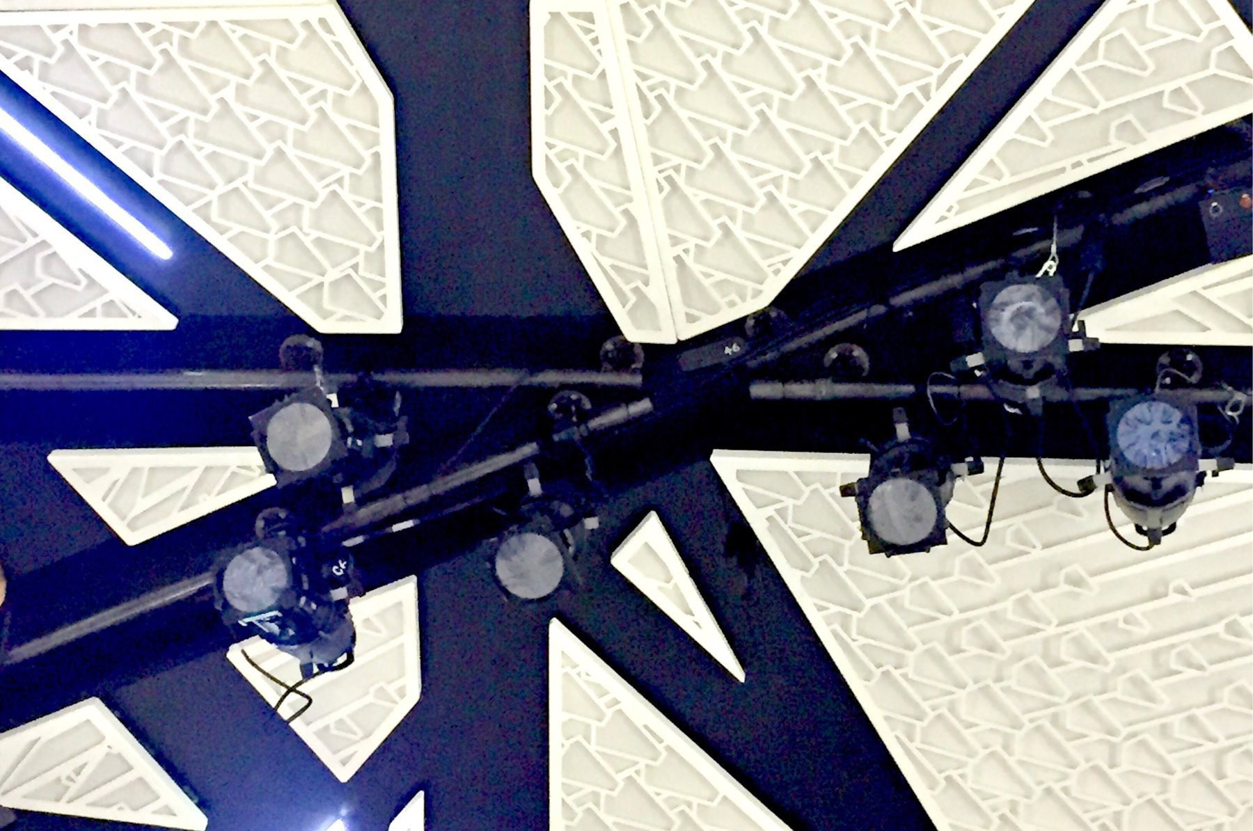 Looking up at several theatrical lights with a white architectural background.