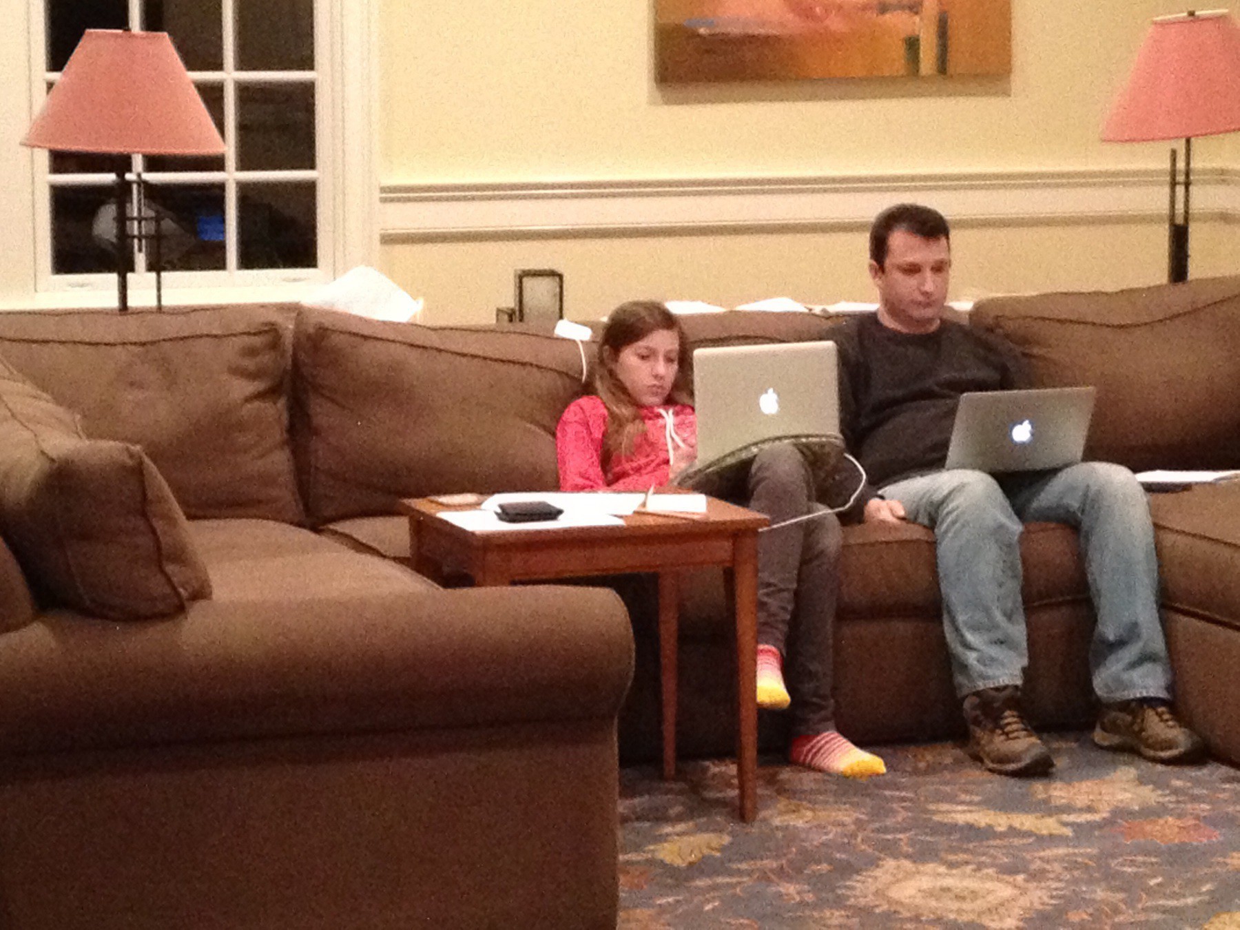 Father and daughter sitting next to each other on a couch. They are both completely focused on their laptops.