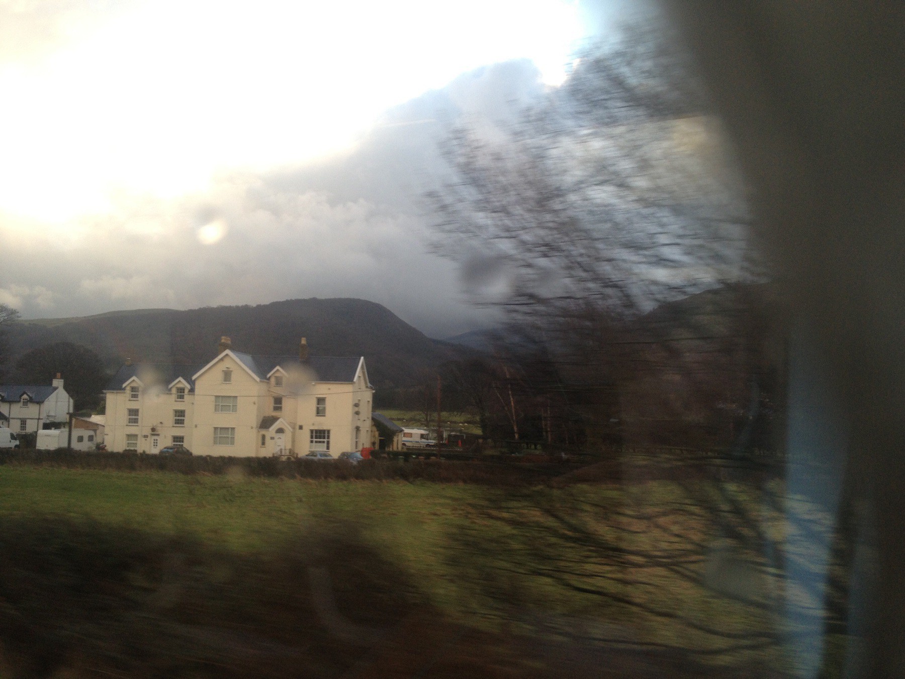 View of manor house, field, and hills through a train window.