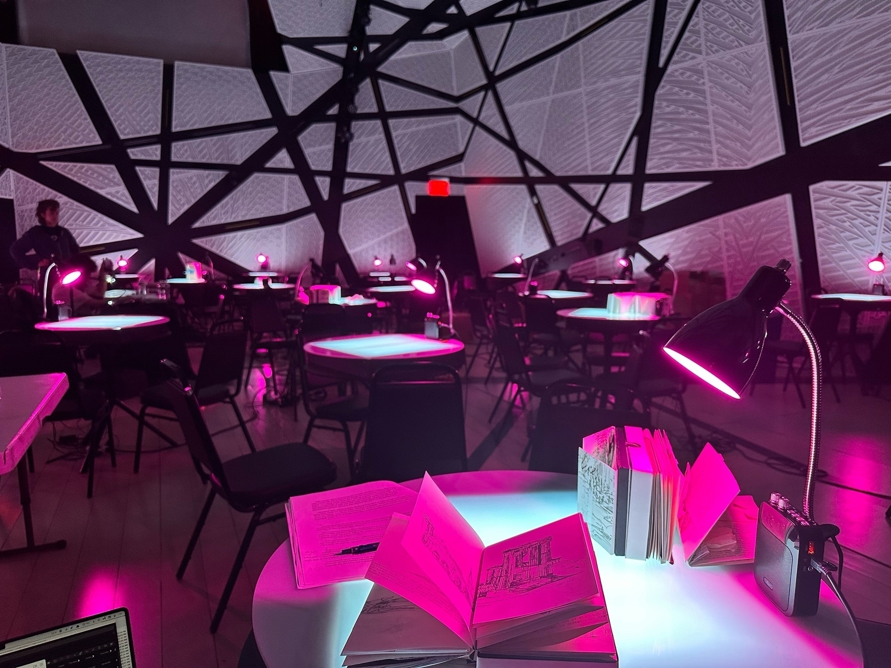 Photo of a white room filled with glowing tables and pink table lamps. 