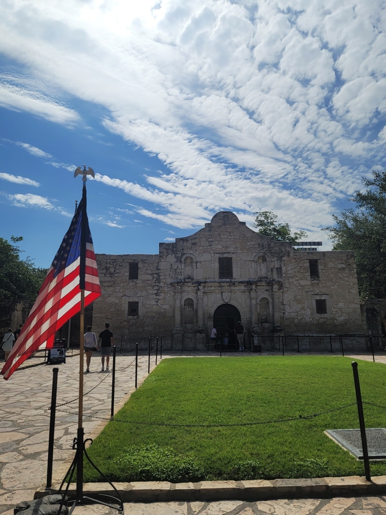 entrance to the Alamo with a small green lawn in front and a blue sky with white clouds