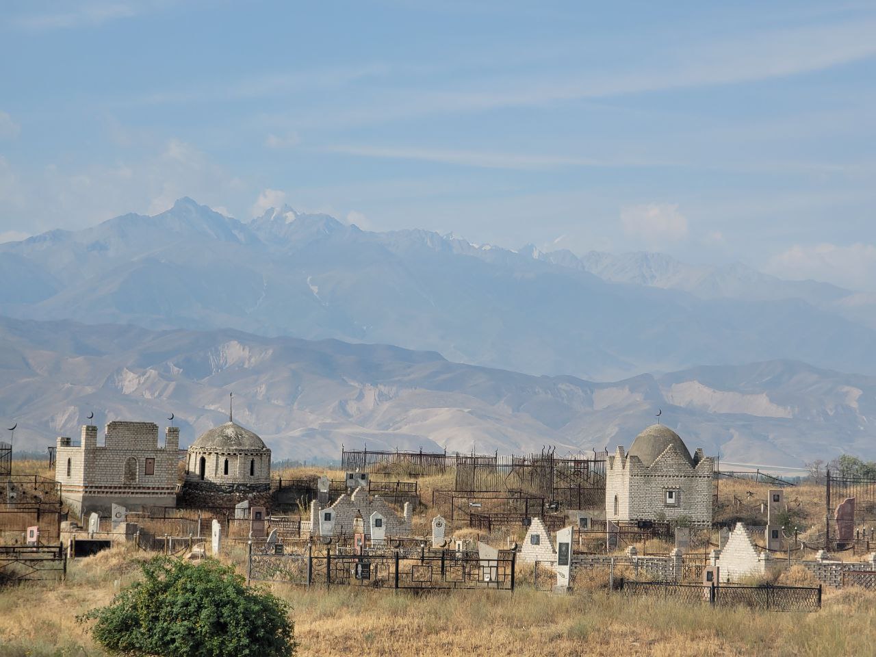 from afar - tombstones inside fenced plots and three small mausoleums. mountains in the background