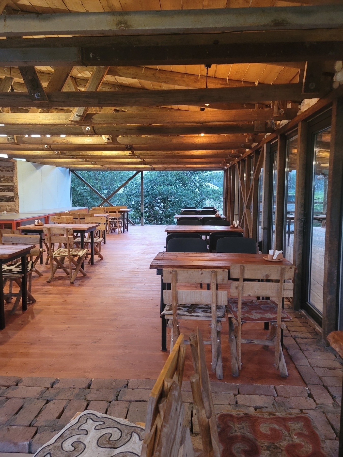 open-air deck area with wooden floor and roof and two rows of mostly wooden tables and chairs