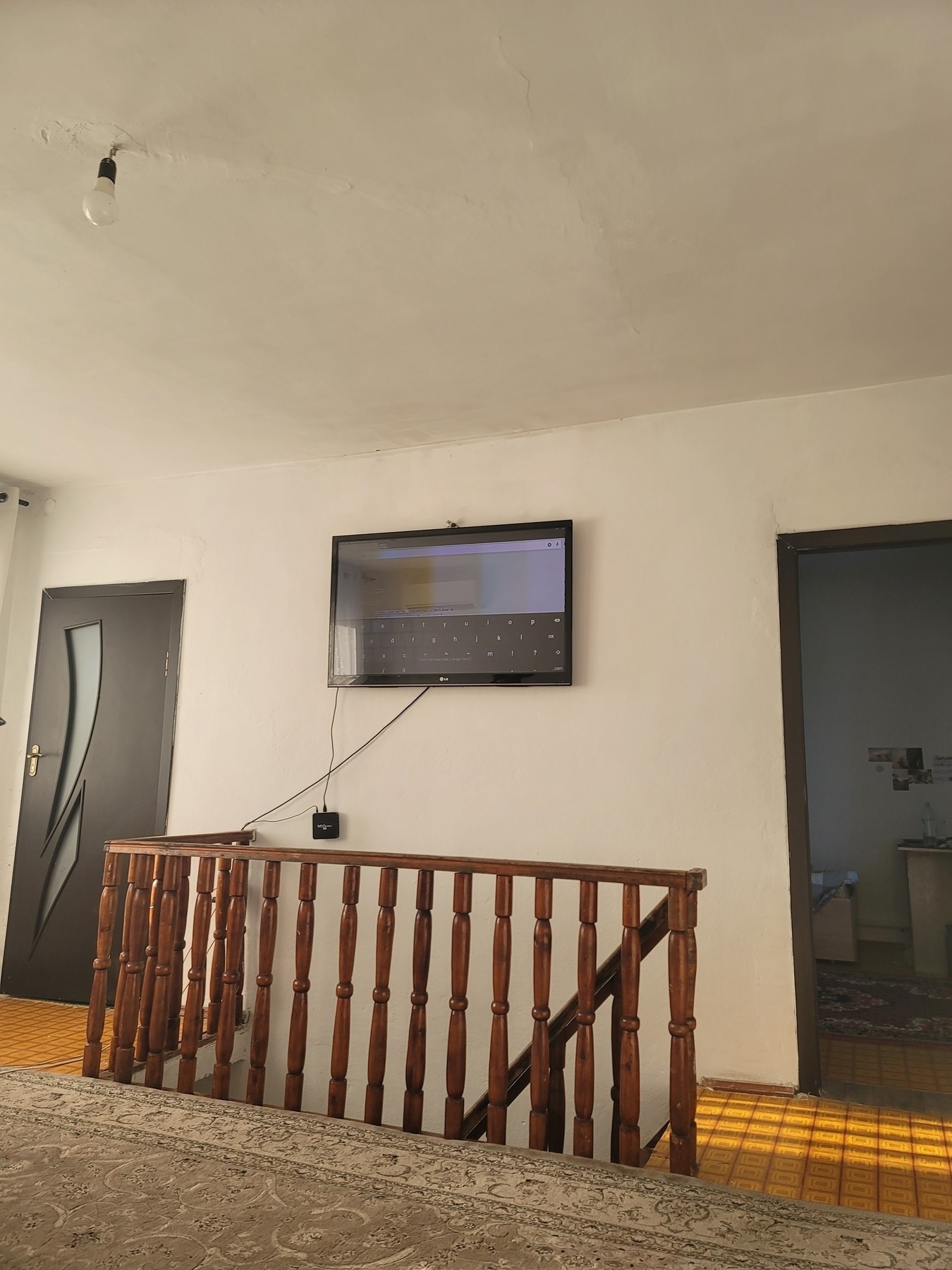 room with a TV hanging on a wall over the rails of a wooden staircase leading downstairs