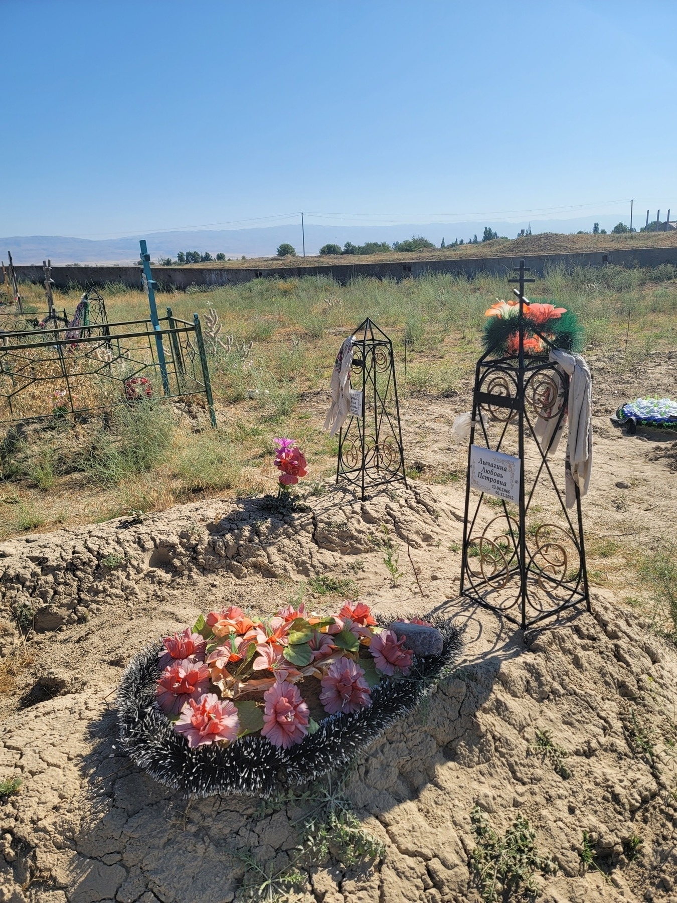 grave mounds, some decorated with flowers, with short wrought-iron towers as headstones and all but one surrounded by fence