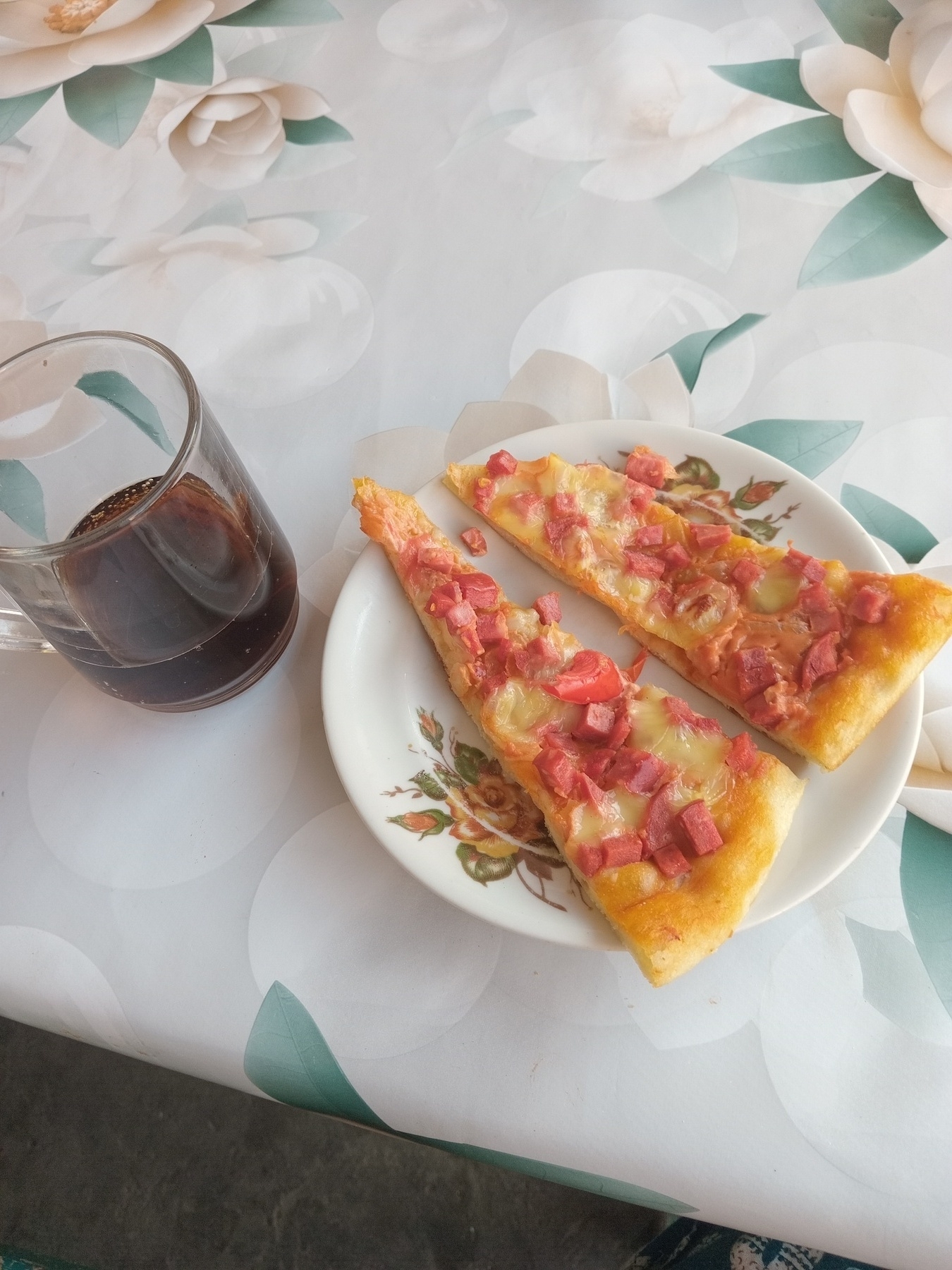 a small glass of mug of coca-cola on the left, plate with two small pieces of pizza on the right 