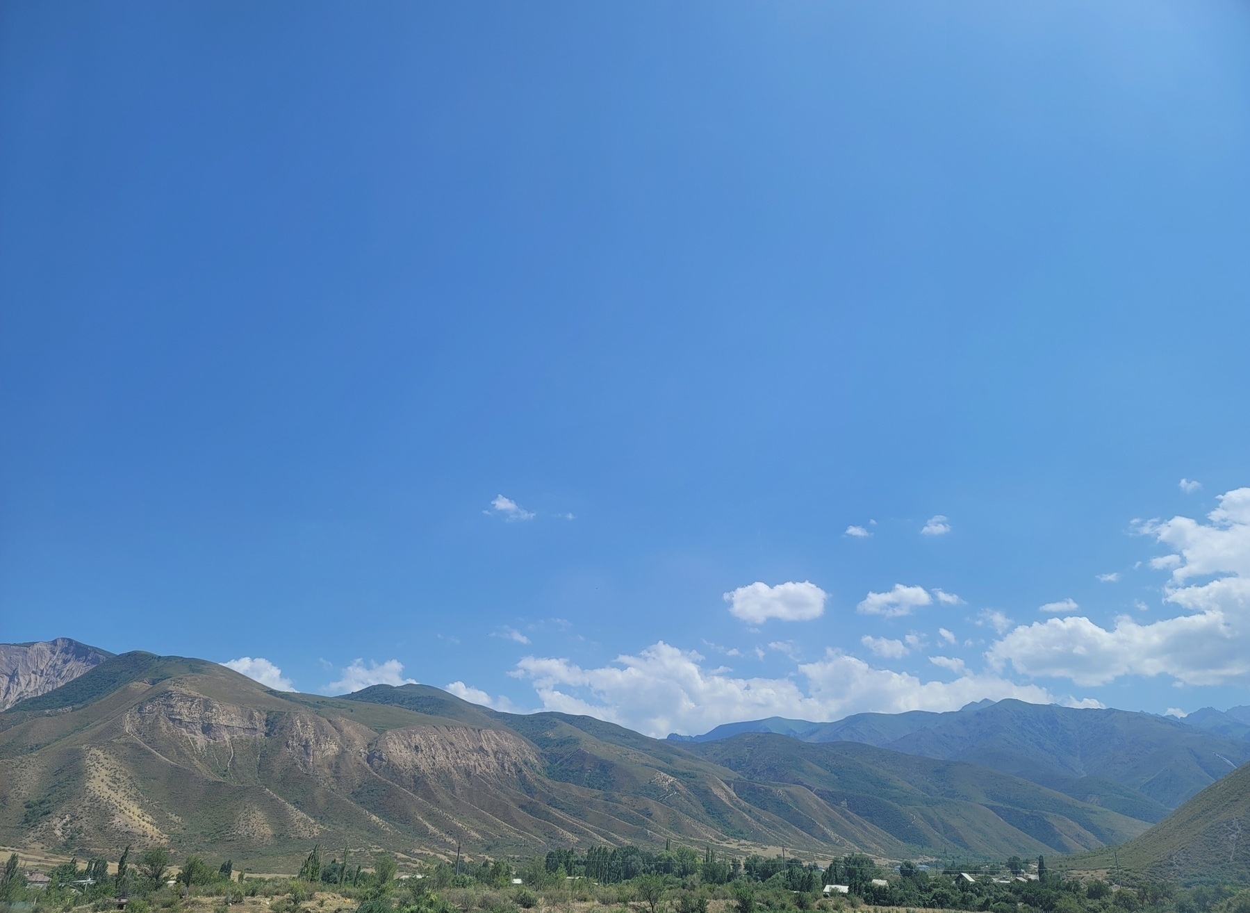green and brown mountain valley under a blue sky with some white clouds