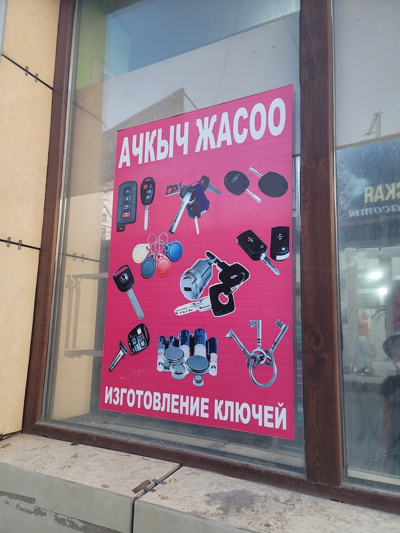 red sign with white text on the top reading 'make keys' in Kyrgyz, white text on bottom with the same in Russian, and pictures of keys in the middle