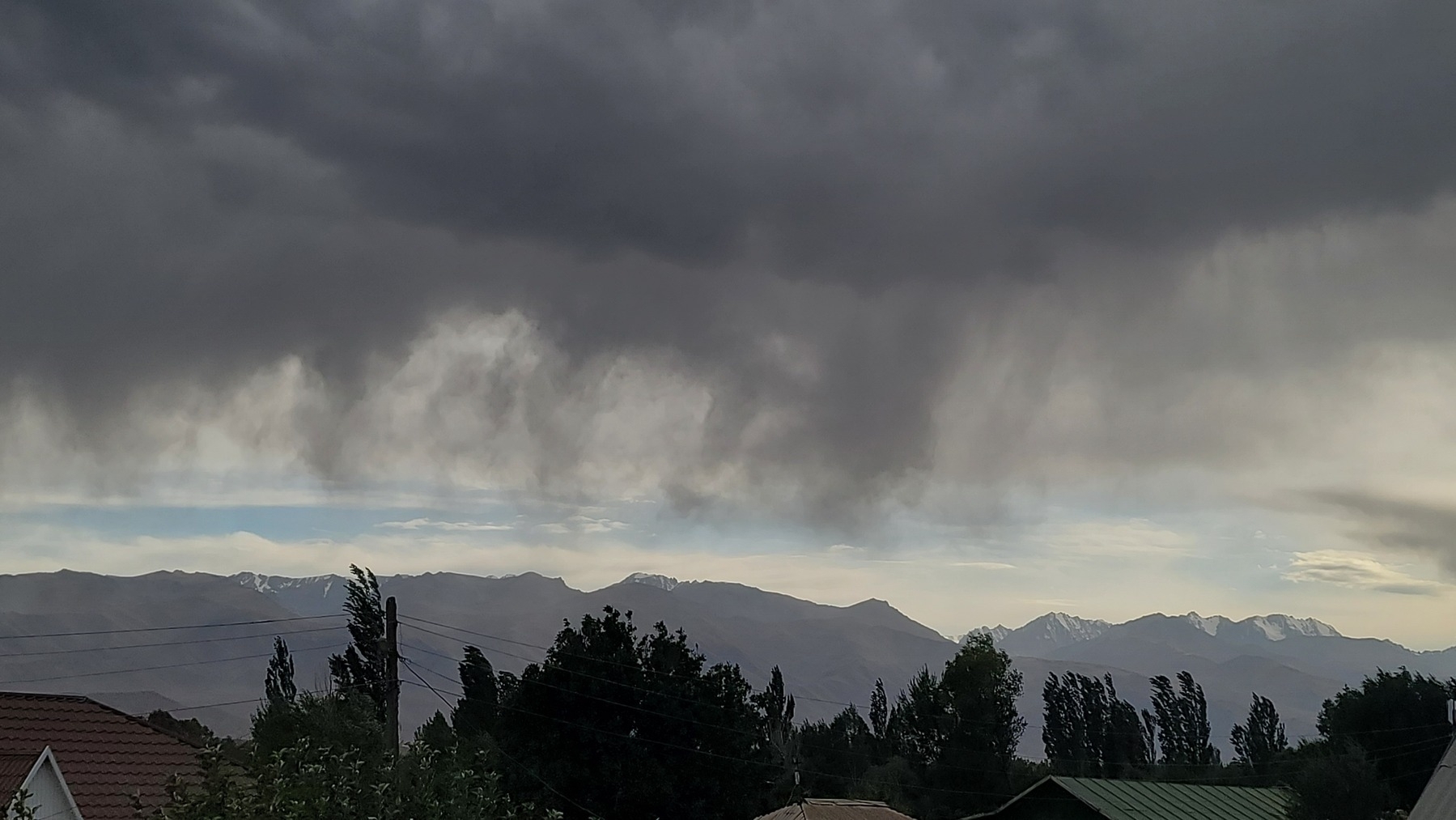 gray rain clouds over mountains in the distance. trees and rooftops closer to the foreground