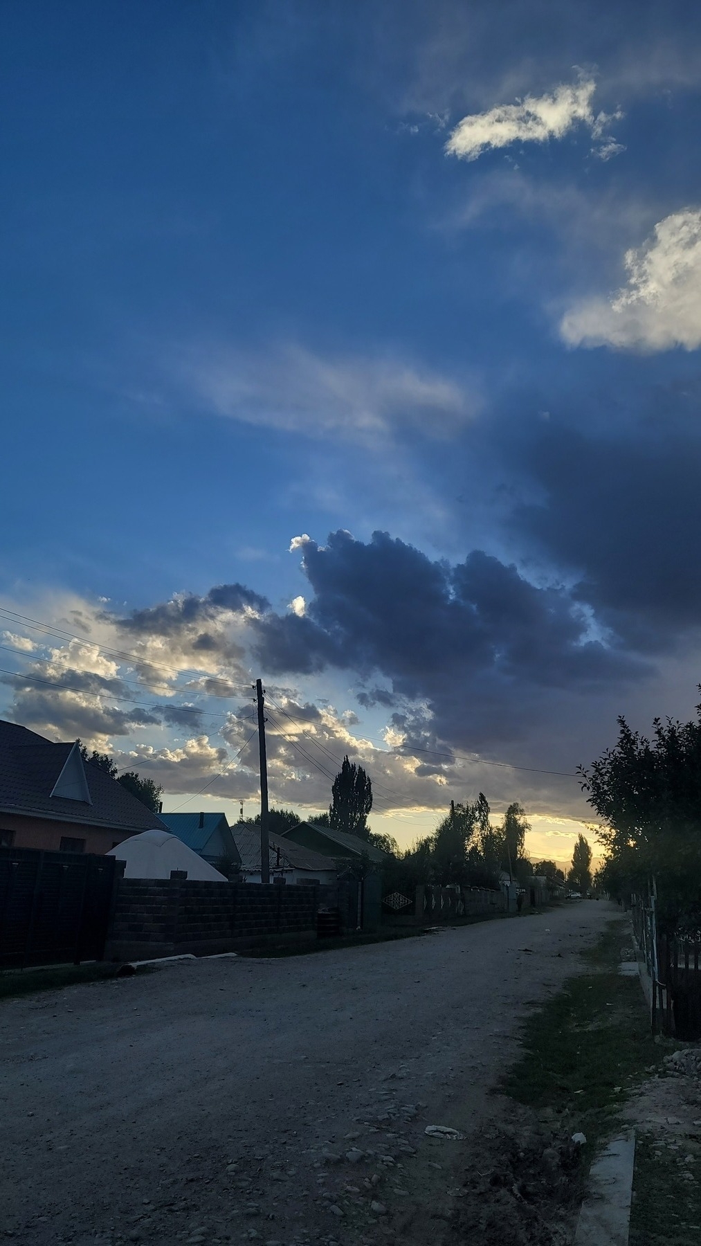 dark clouds in front of a bright sun, shortly before sunset. street with houses extending into the distance