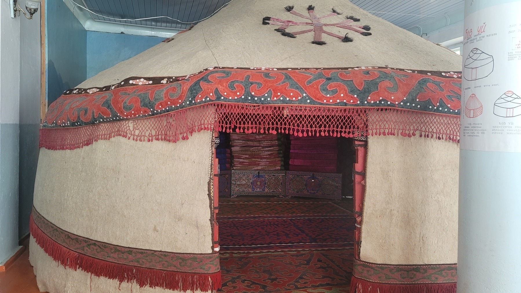Kyrgyz felt yurt set up inside a room with chests, rugs and blankets visible inside