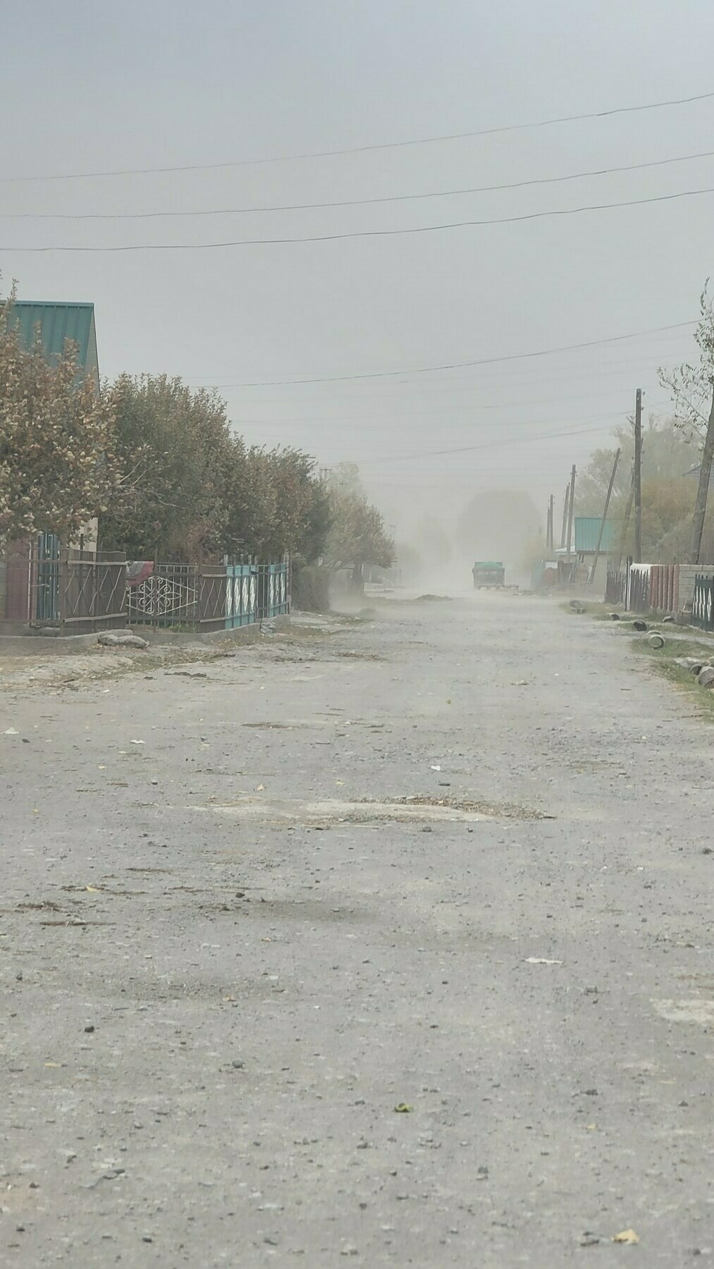 down a dirt road in a neighborhood, air looks gray-ish and the sky is not clear because of all the dust 