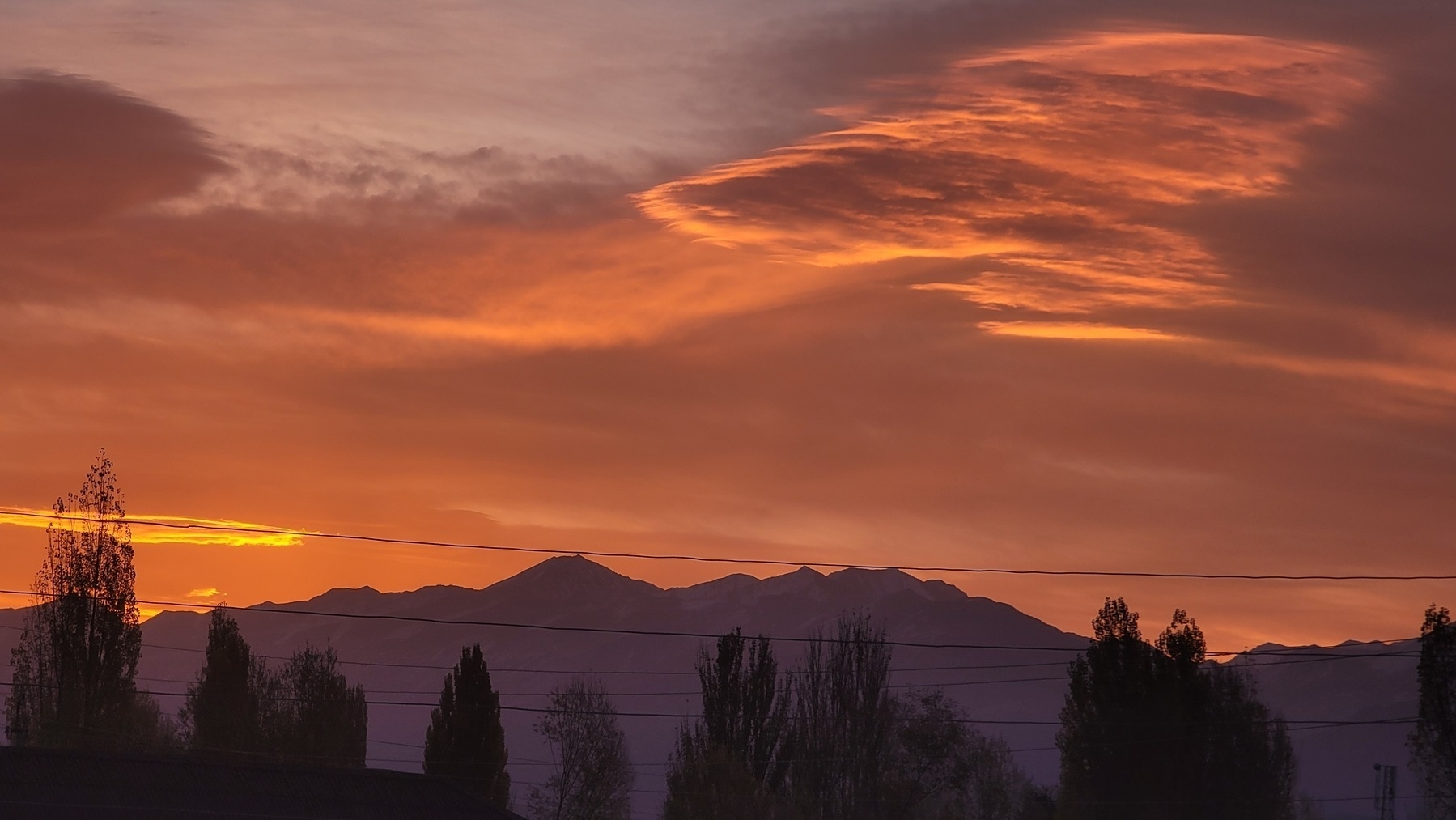 orange/purple sky/clouds and mountains in the background; trees and powerlines in the foreground 