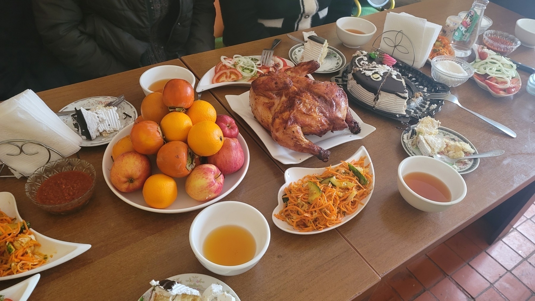 table with various plates: rotisserie chicken, cake, fruit, vegetable salads, tea