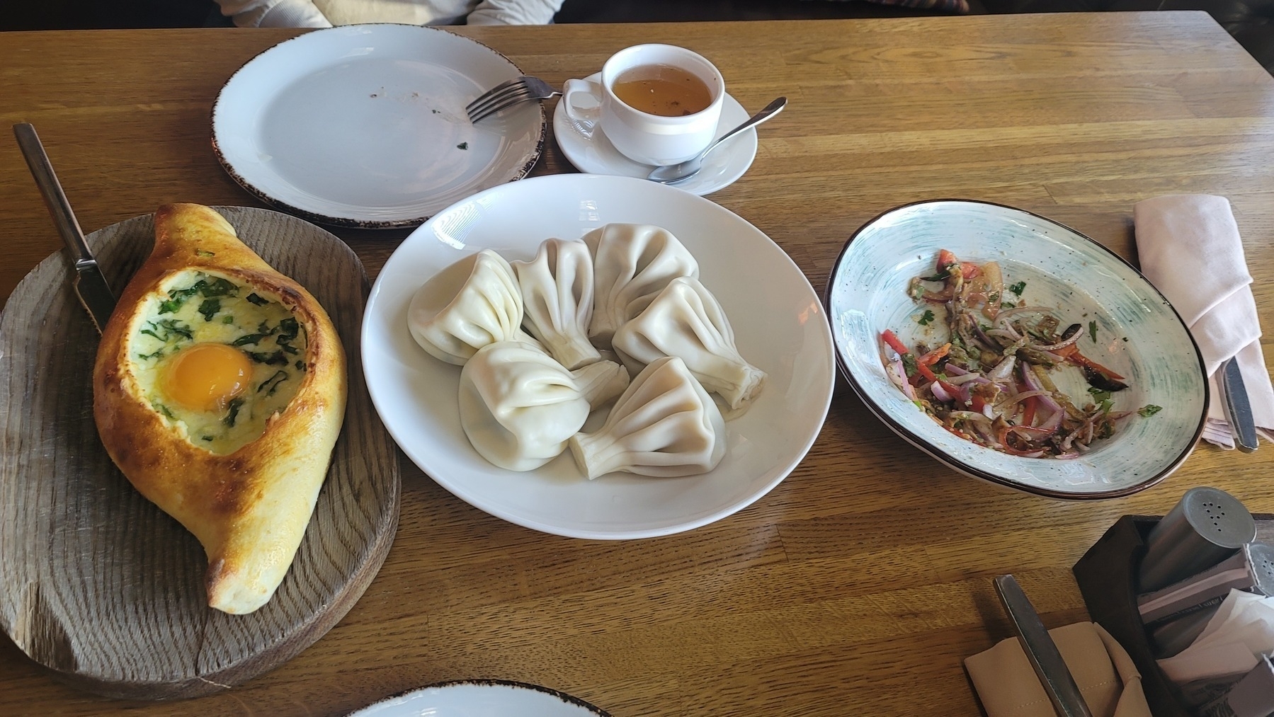 khachapuri (bread with a lowered part in the middle filled with an egg, cheese and spinach ), plate of 6 khinkali, tea and half of a salad on a table 