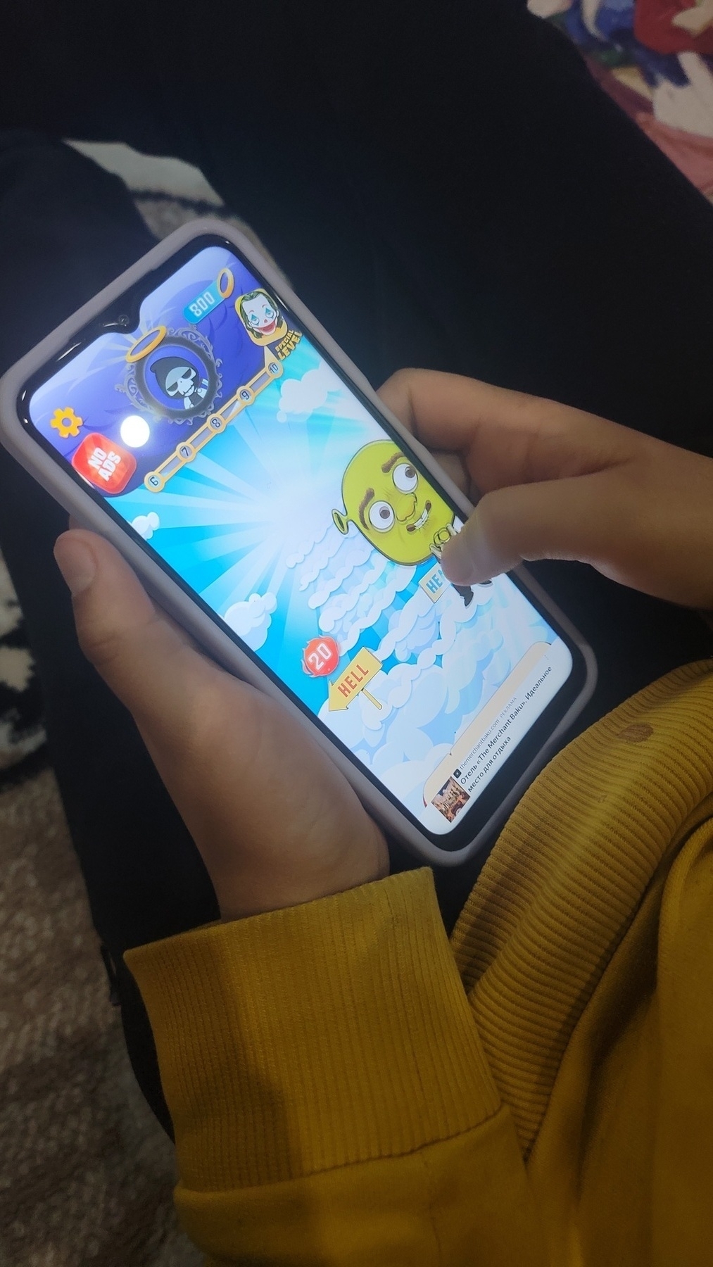 person with a phone in their hands. game open with left side of screen labeled as Hell (right as Heaven, but not visible). user is dragging a cartoon version of Shrek to the Heaven side