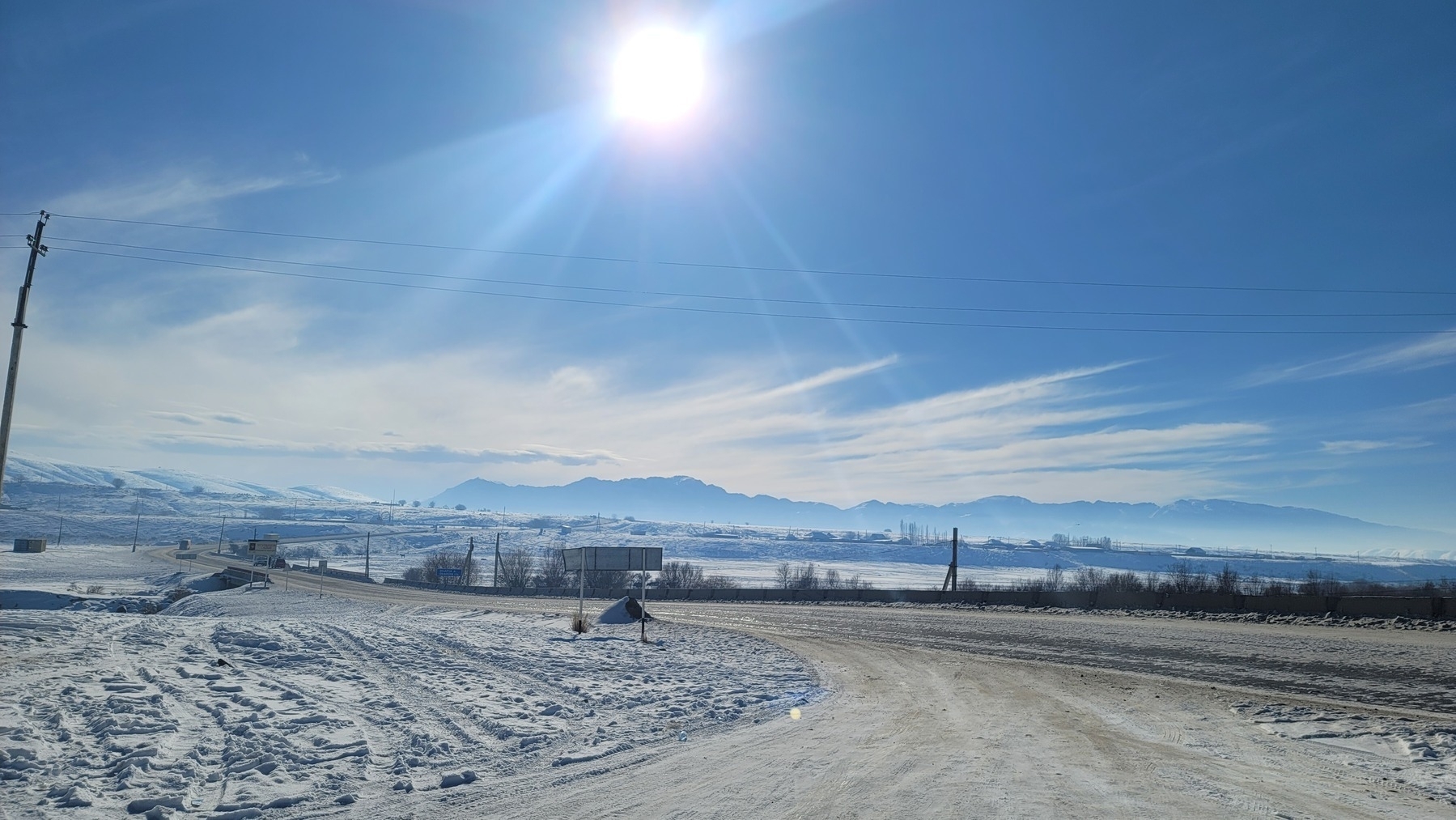 road extending into the distance with snow on either side and mountains in the distance on a clear, blue, but cold sunny day