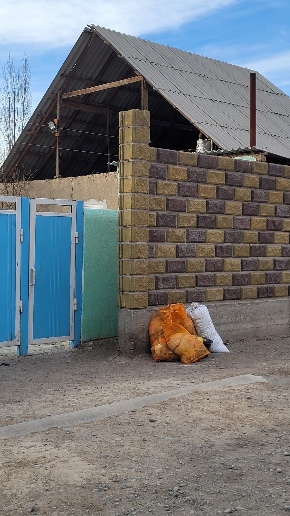 three orange mesh sacks and one white sack leaning against a two-color brown brick wall and blue gate of a house