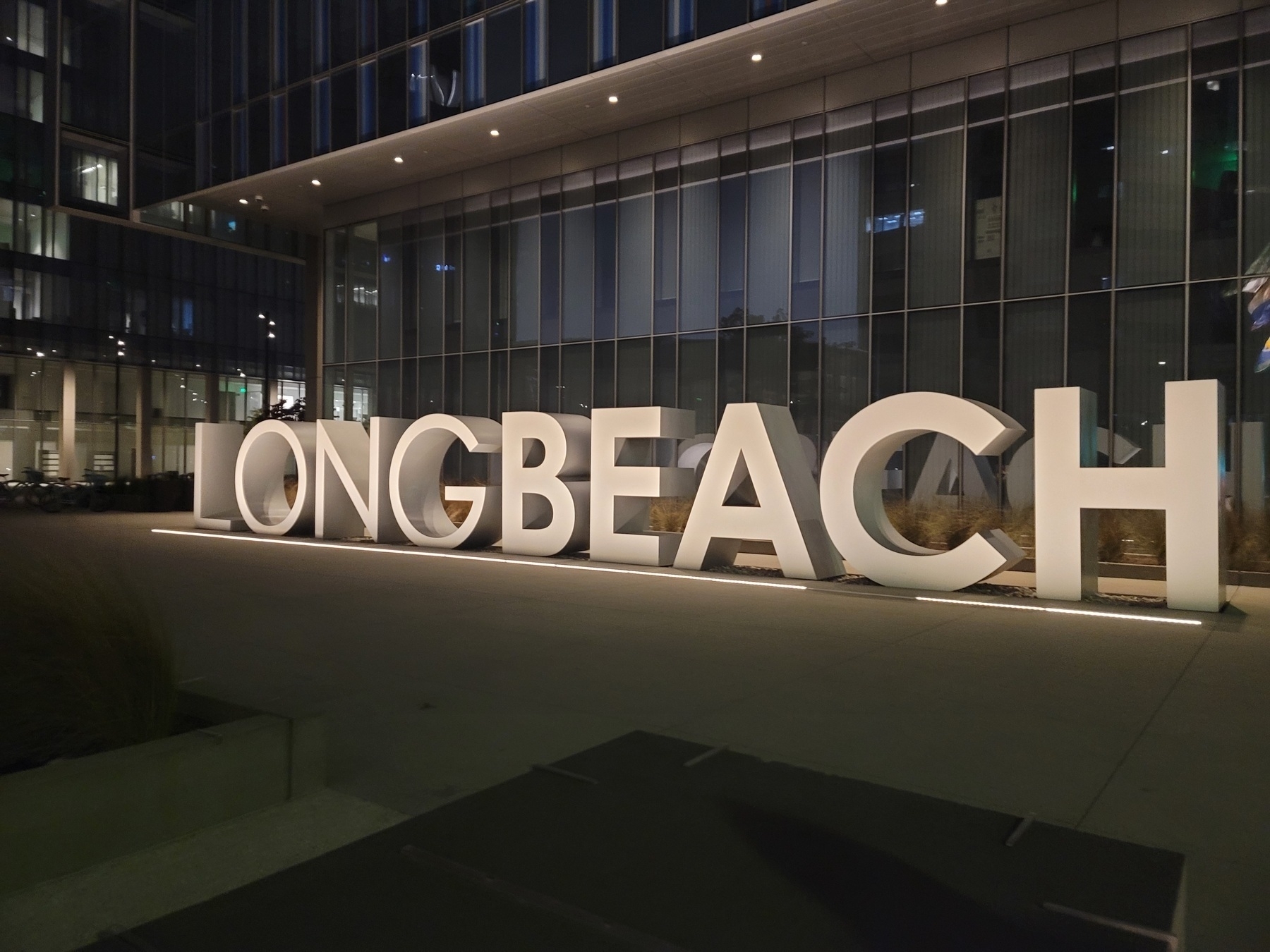 giant, white 3-D block letters spell out "LONG BEACH" outside of a glass building at night