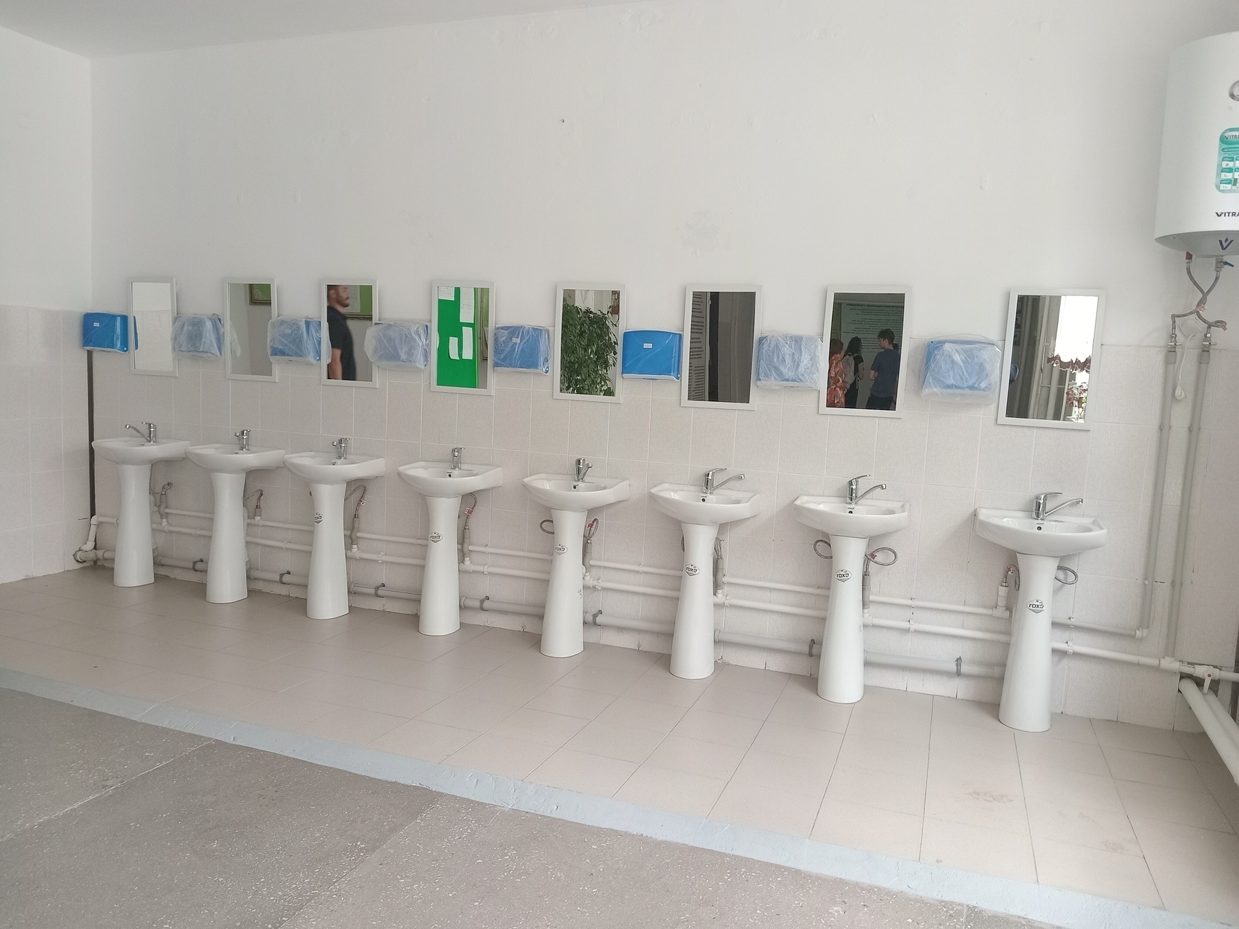 row of 8 white sinks against a wall, each with a small rectangular mirror above it