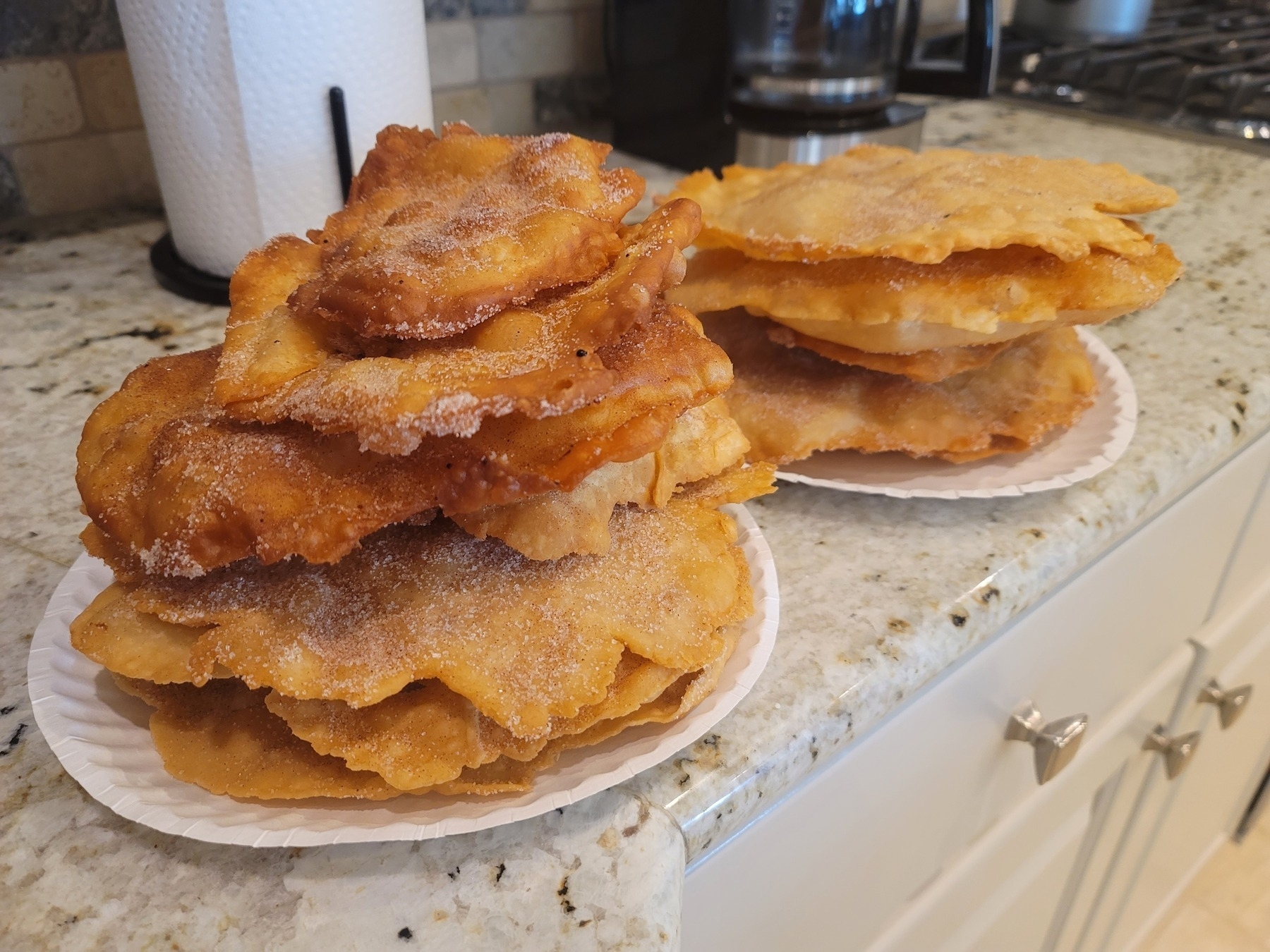 mostly pancake-sized buñuelos chips dusted with cinnamon and sugar stacked on two plates