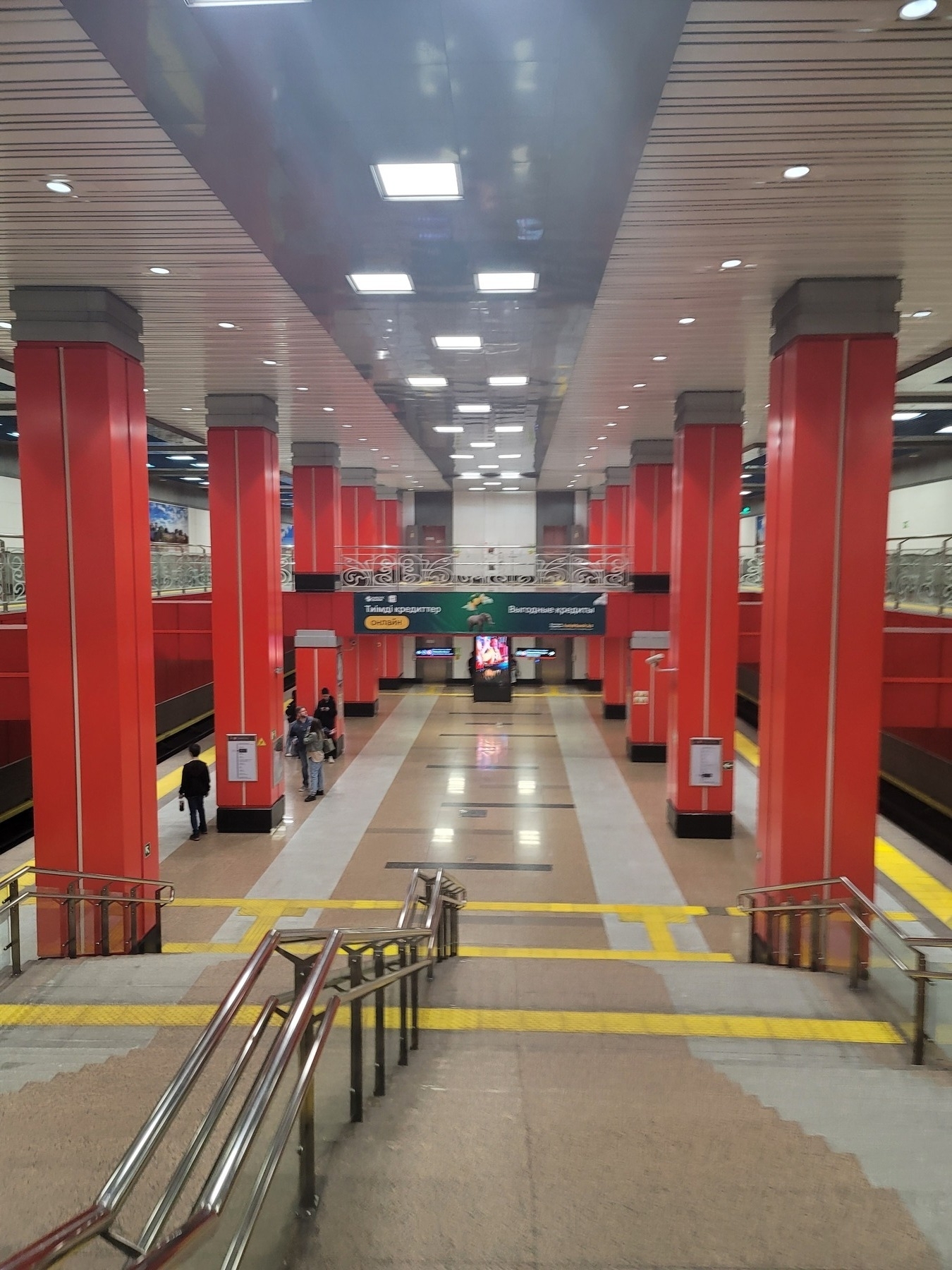 bright metro station with red orange columns; picture taken from stairs leading down to where metro trains come