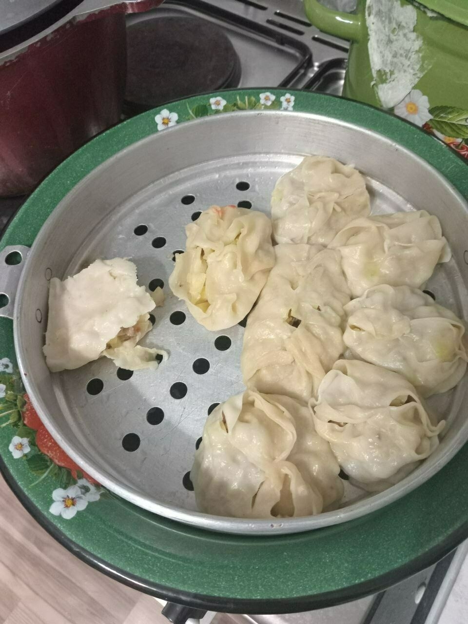 8 dumplings in a gray steamer dish in a green, ceramic bowl sitting on the stovetop