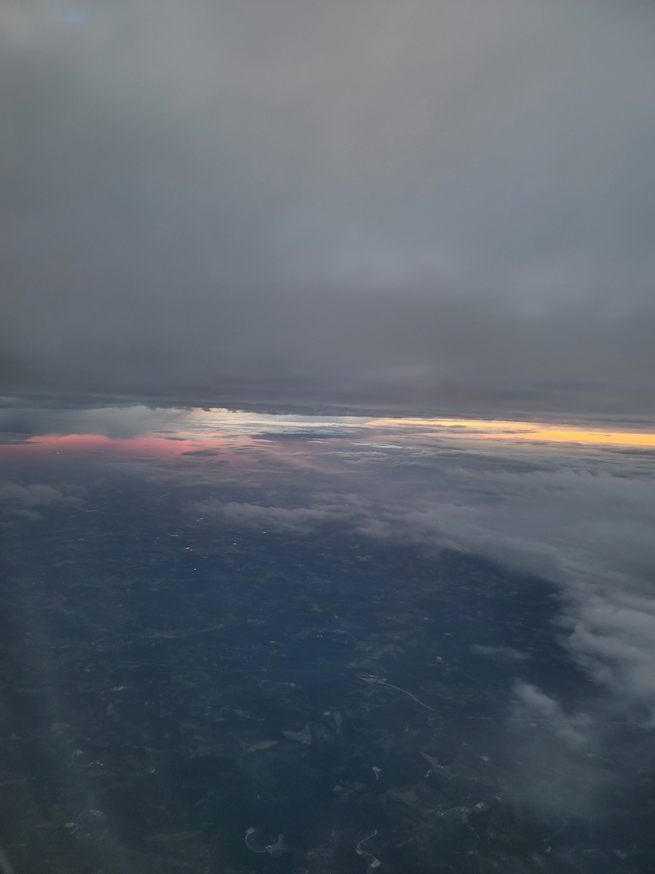 gray clouds but in center of image a break on the sky - a streak of pink on the left and a streak of orange on the right. mass of trees visible in lower left corner