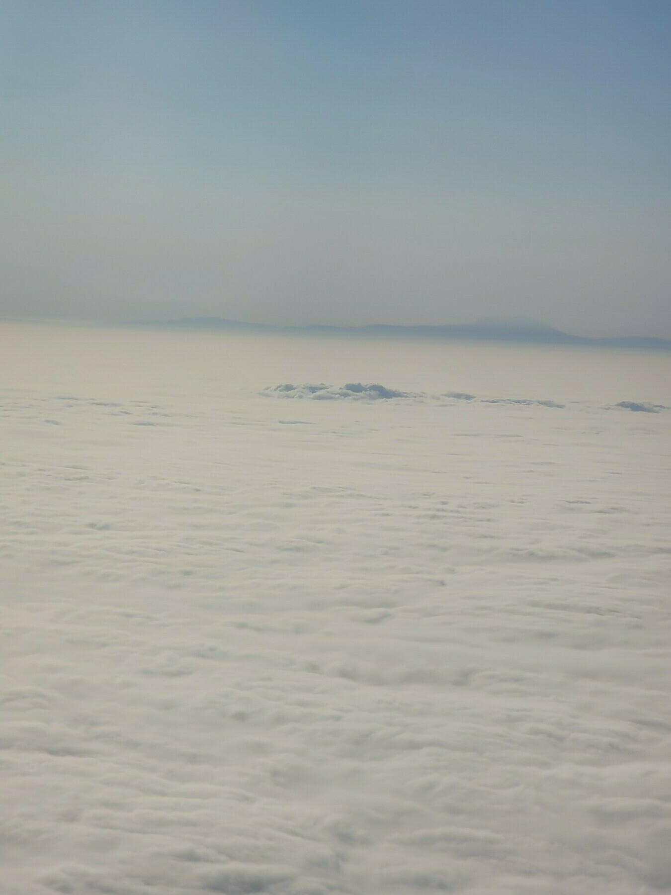 sea of clouds from an airplane window with mountains visible in the background