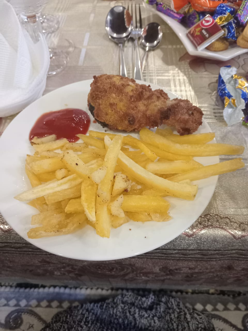 white circular plate with ketchup in the top left corner, chicken wing in the top right corner, and fries on the bottom half