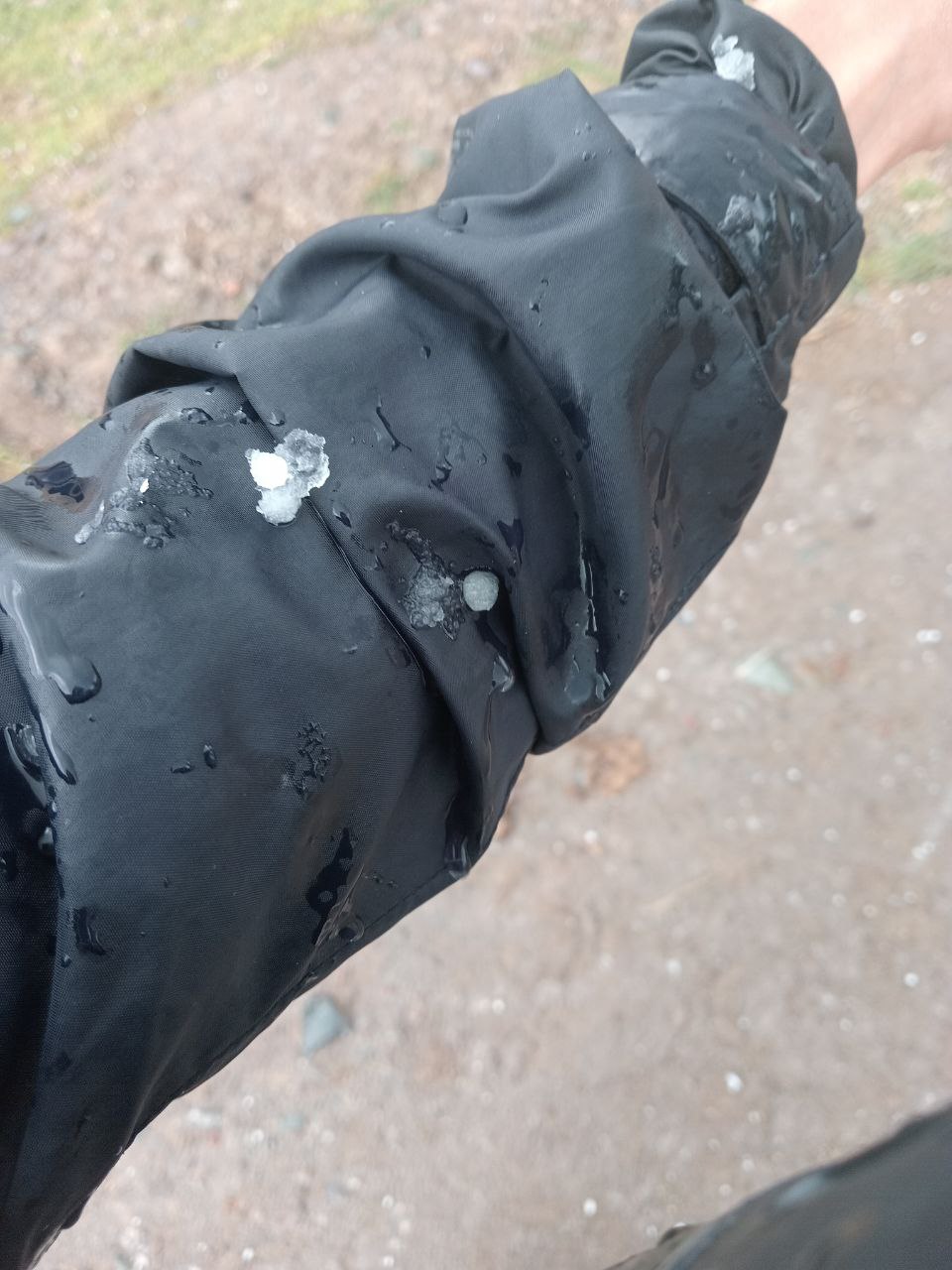 black nylon raincoat sleeve (being worn) extended out, with a few bits of ice on it