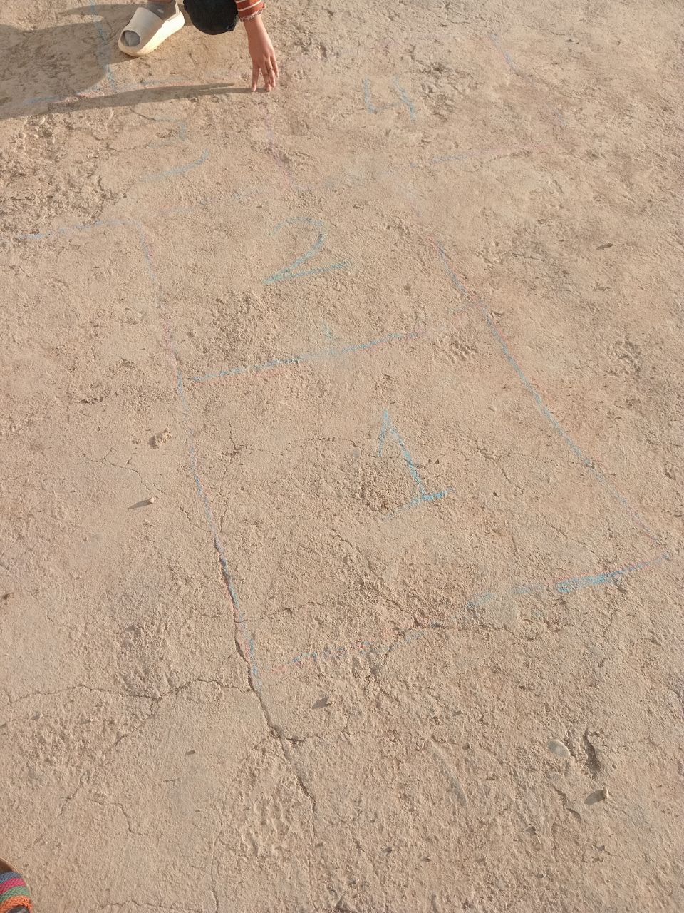 light brown rocky ground with 3 faint blue chalk hopscotch spaces labeled with numbers drawn on it