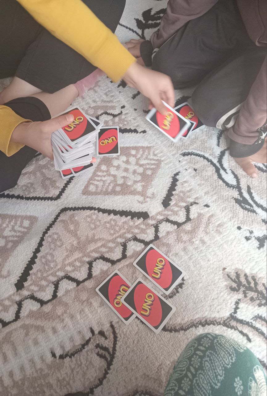 three people sitting on a floor with Uno cards (faces not visible, only feet, arms and legs)