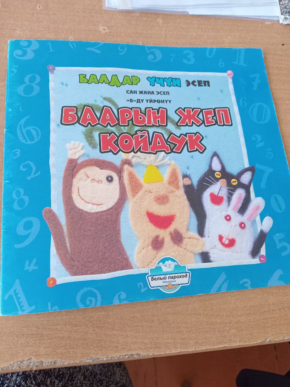 blue picture book with a sewn, felt-style monkey, pig, cat and rabbit drawn on the front. title in Kyrgyz: баарын жеп койдук