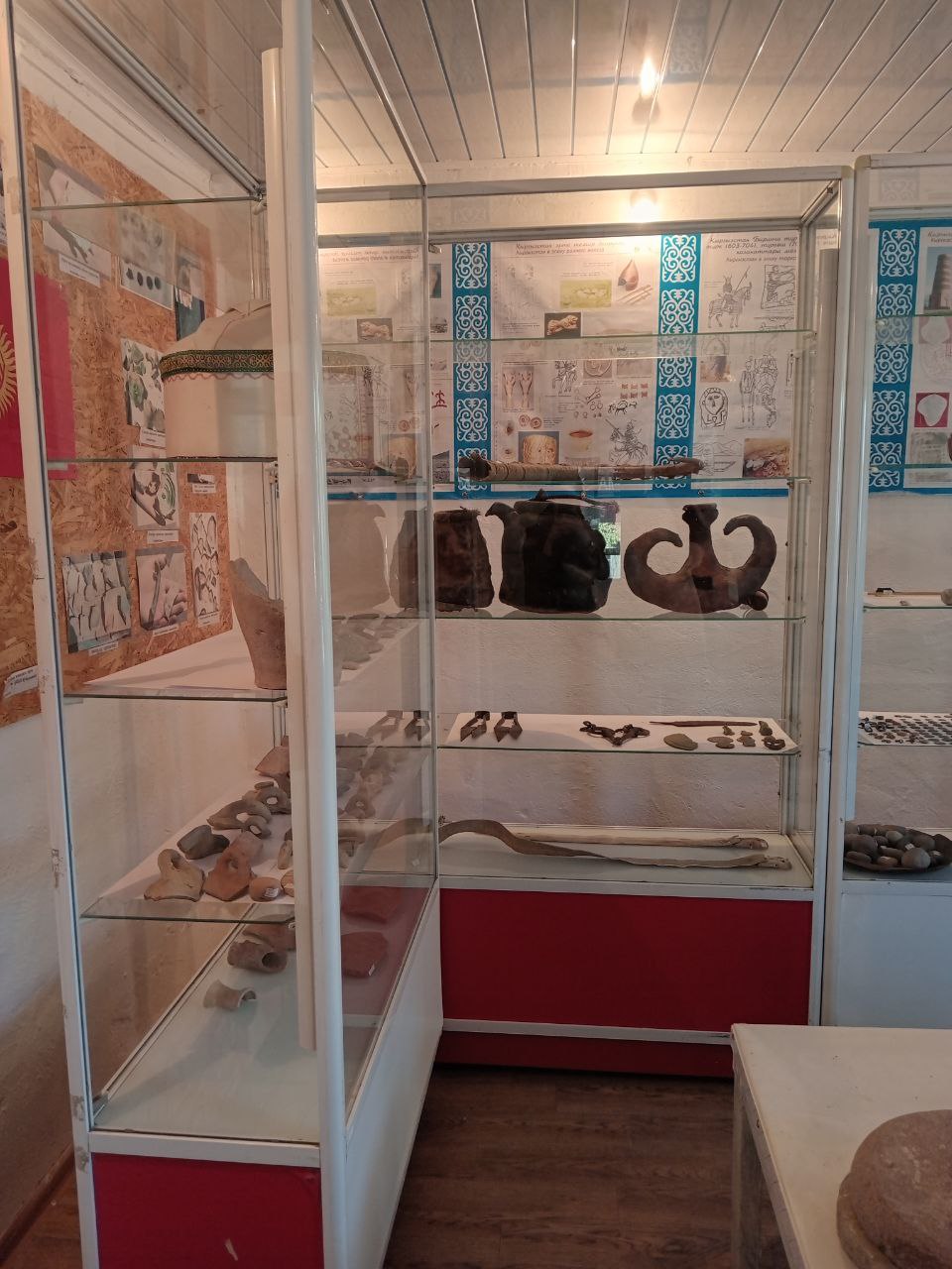 corner of a room. glass display cases with various old artifacts inside and posters on the walls