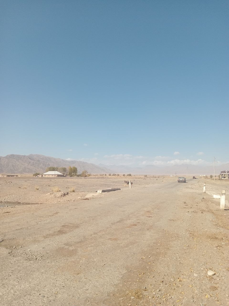 dirt road with a car on it in the distance; mountains closer to the foreground on the left but also in the background 