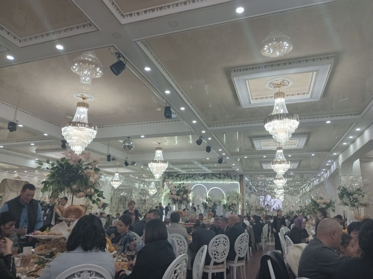 big, fancy banquet hall with round tables and people sitting around them 