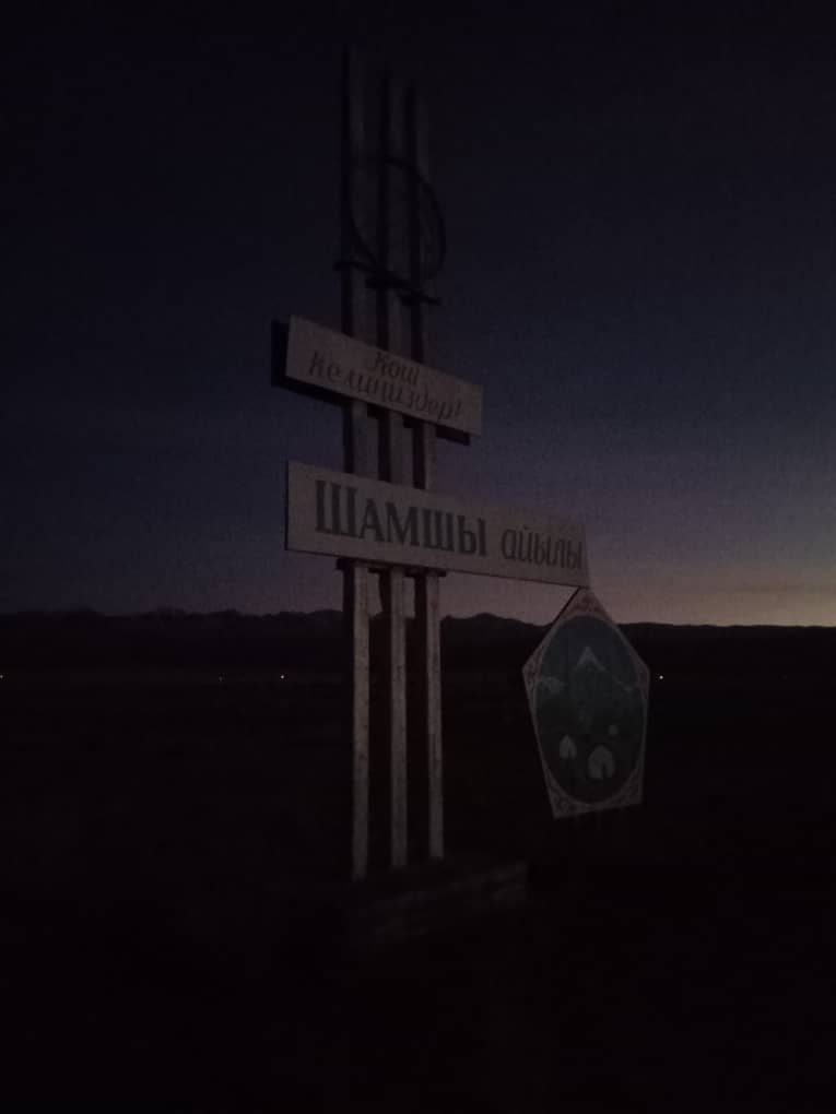 a sign at sunrise which says "welcome to Shamshy village" in Kyrgyz