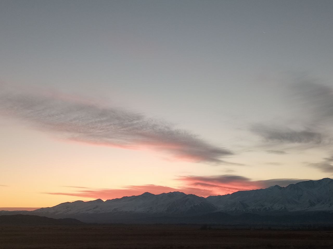 white mountains at sunrise with a couple of pink-orange clouds behind them