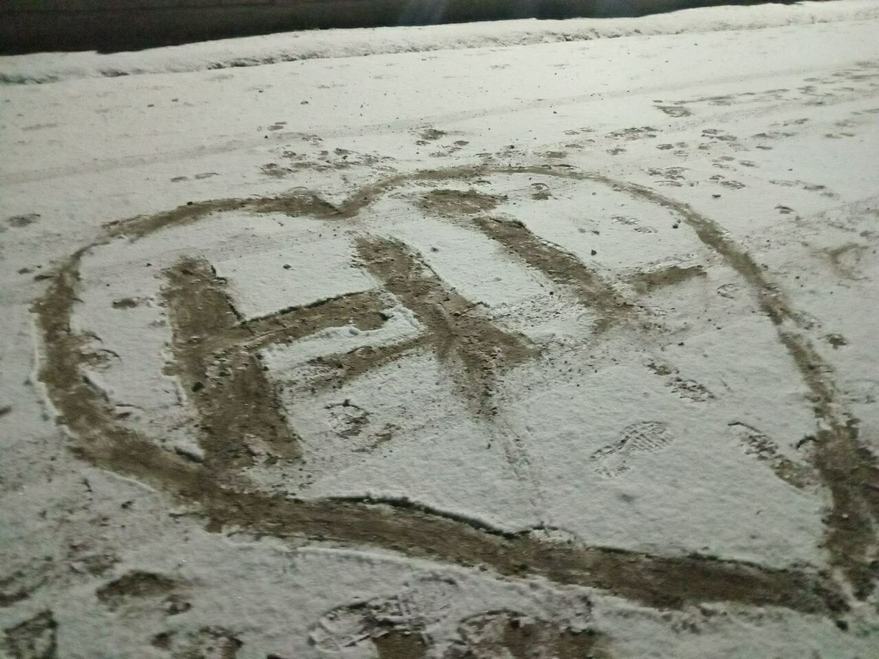 "hi" with a heart around it written in thin snow with mud showing underneath. there's a mark under the horizontal line of the H and a mark to the right of the i where a drunk guy walked through 